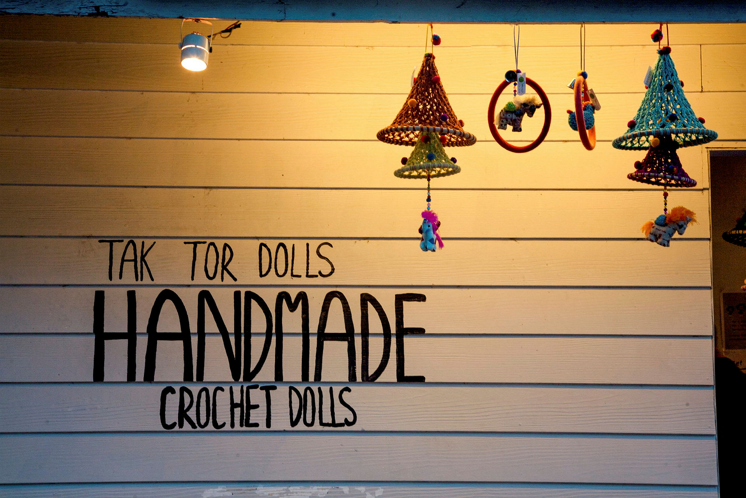 Vägg med texten 'Handmade Crochet Dolls' och hängande virkade dekorationer. (AI-genererad text)