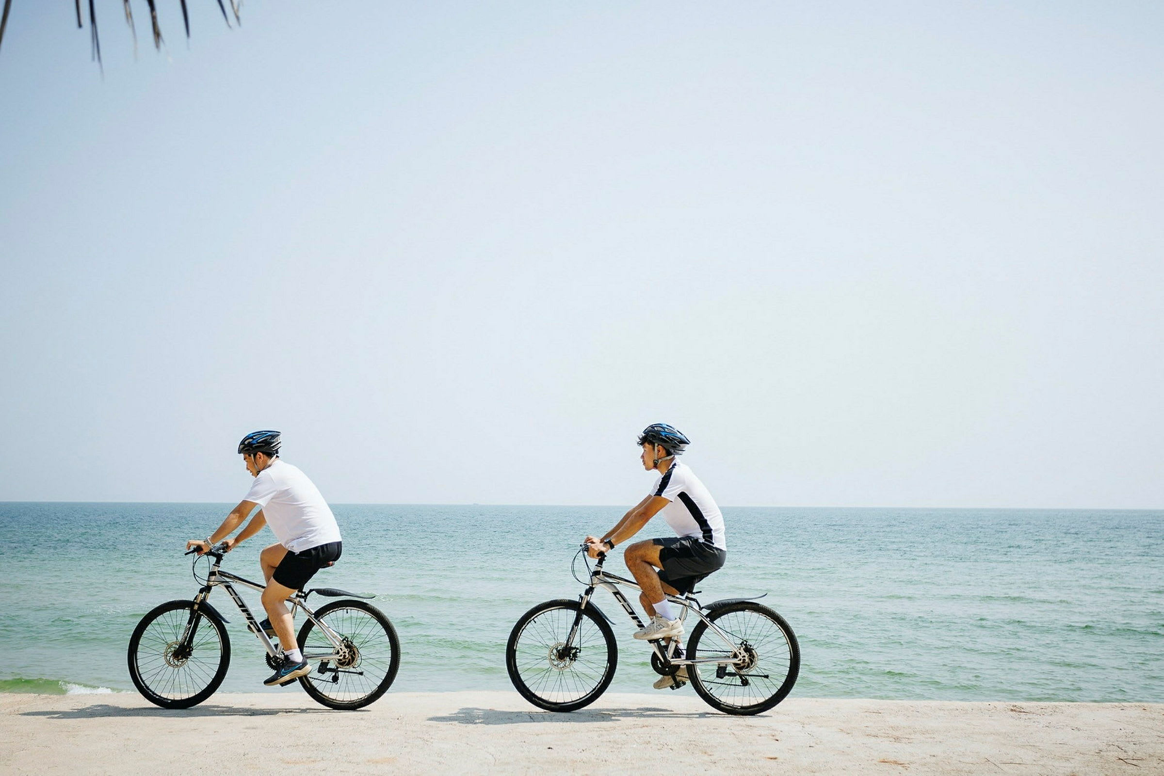 Två personer cyklar vid en strand nära havet. (AI-genererad text)