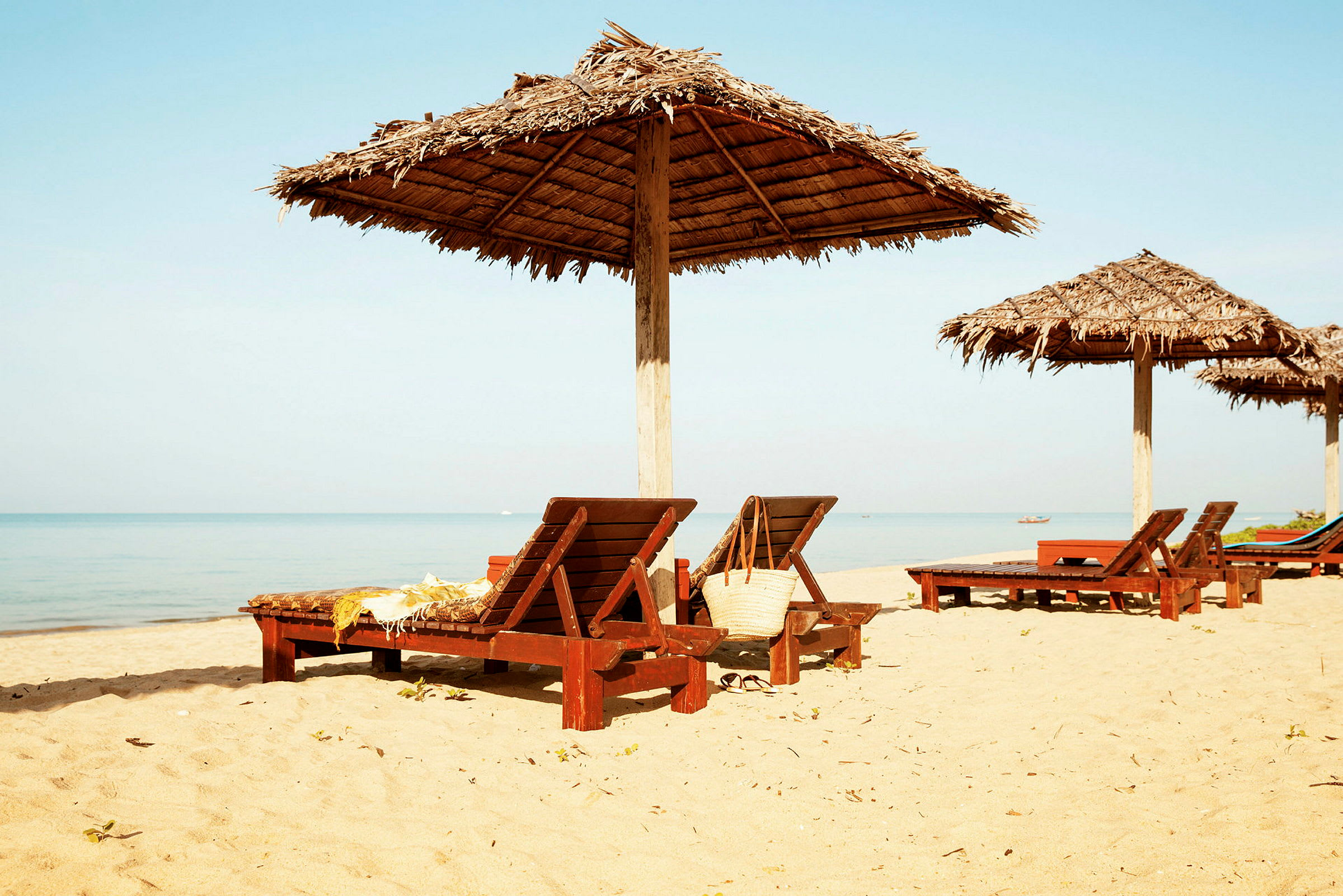 Solstolar på en sandstrand med parasoller i trä. (AI-genererad text)