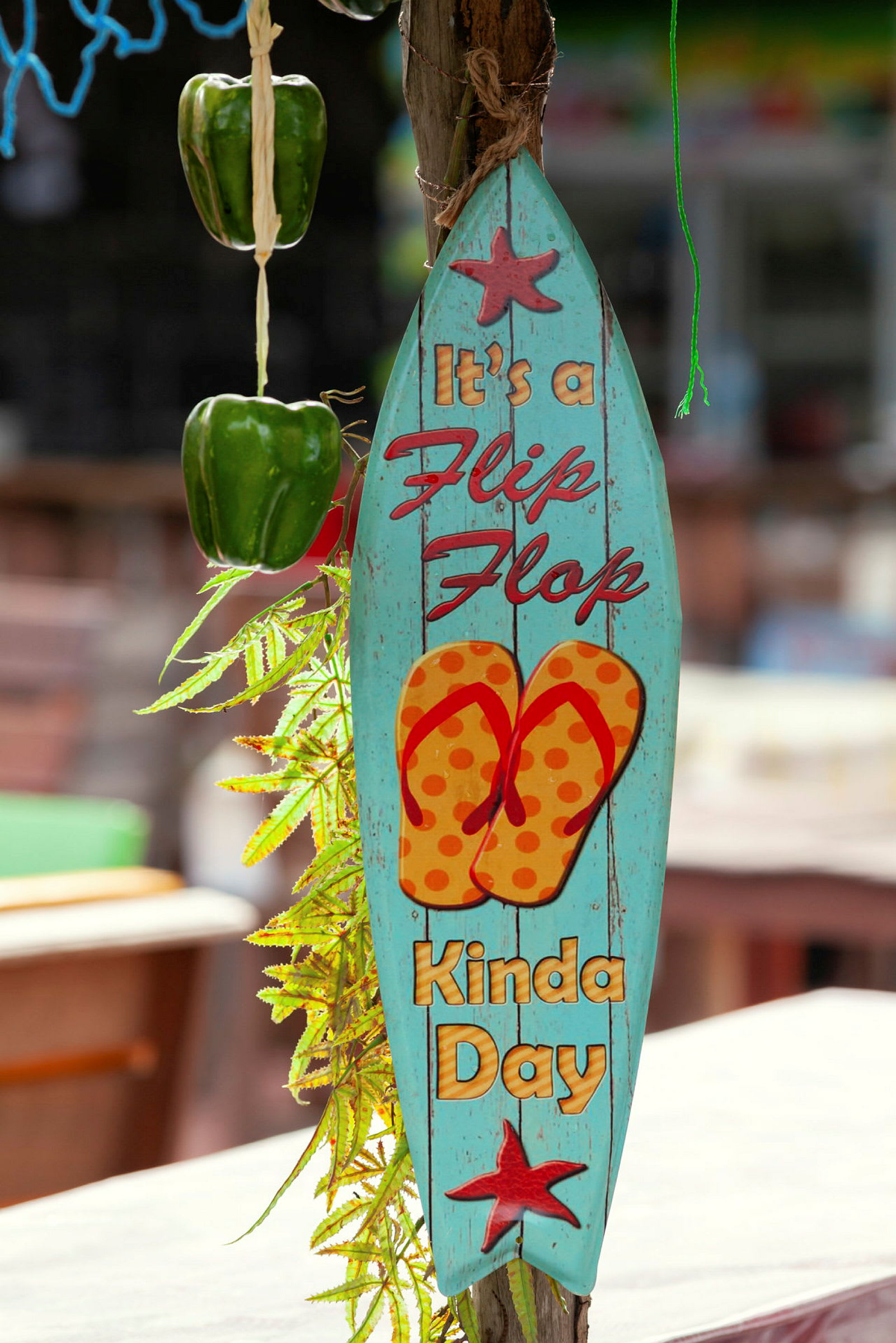 Ett blått skylt med texten 'It's a flip-flop kinda day', en bild av sandaler och dekorerad med stjärnor hänger bredvid grön paprika och gröna blad. (AI-genererad text)