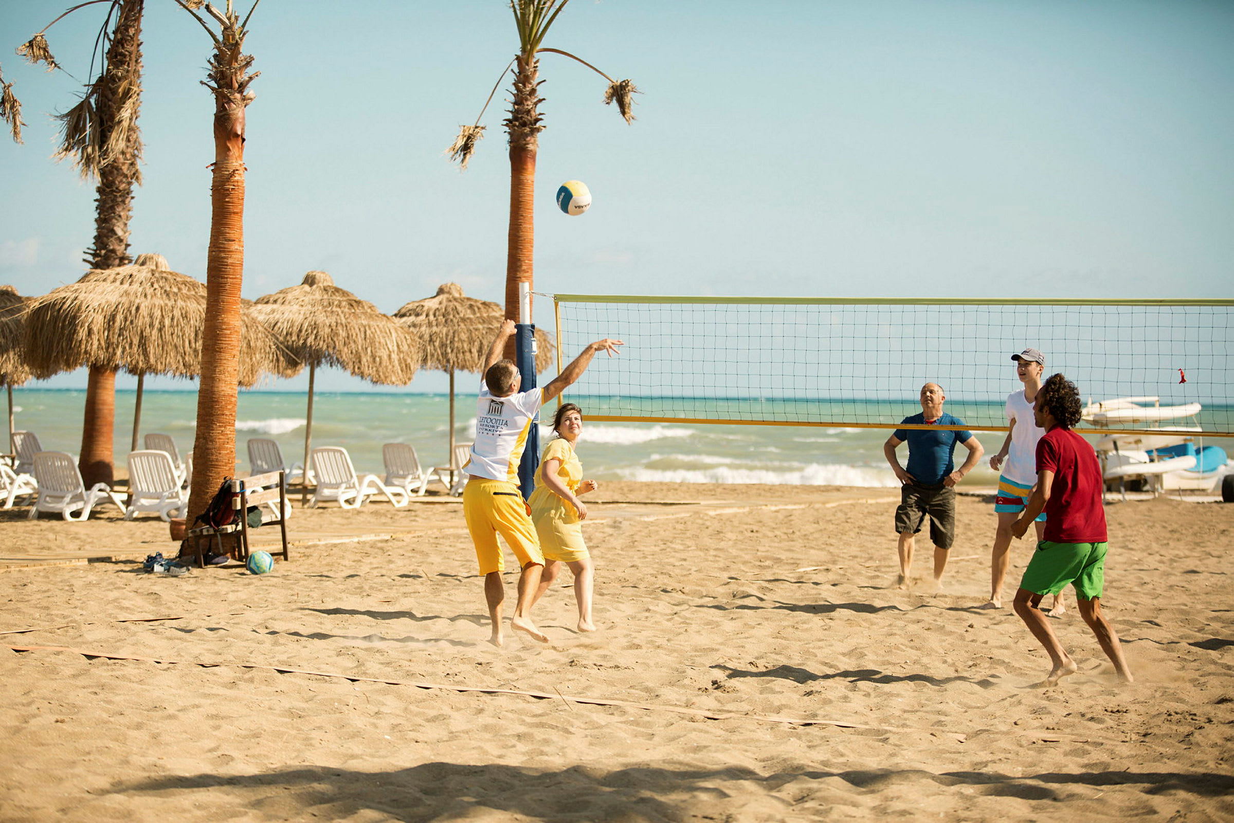 Personer spelar volleyboll på en sandstrand med palmer och hav i bakgrunden. (AI-genererad text)