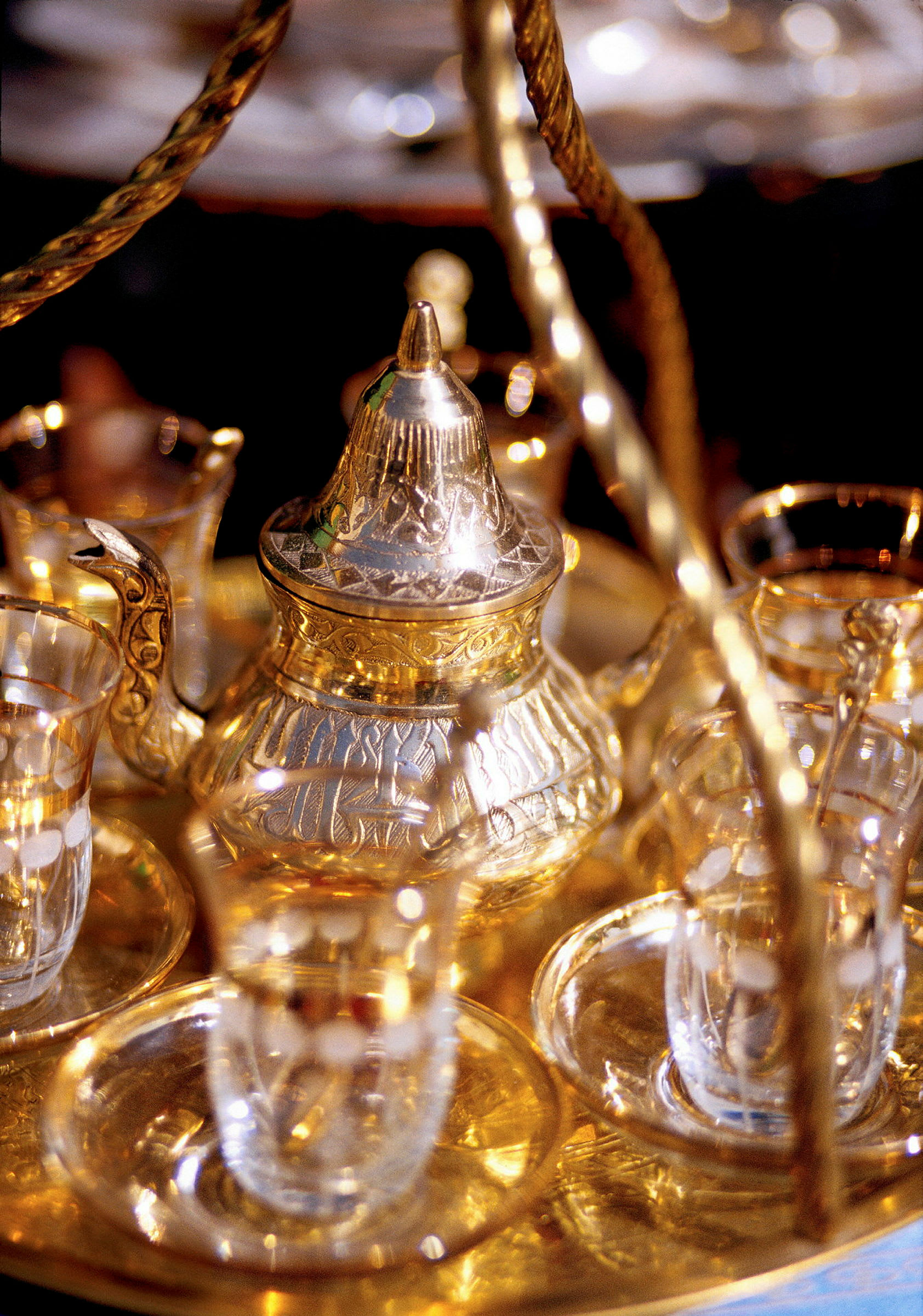 En detaljbild av en dekorativ te- eller kaffekanna i guld med glas koppar. (AI-genererad text)