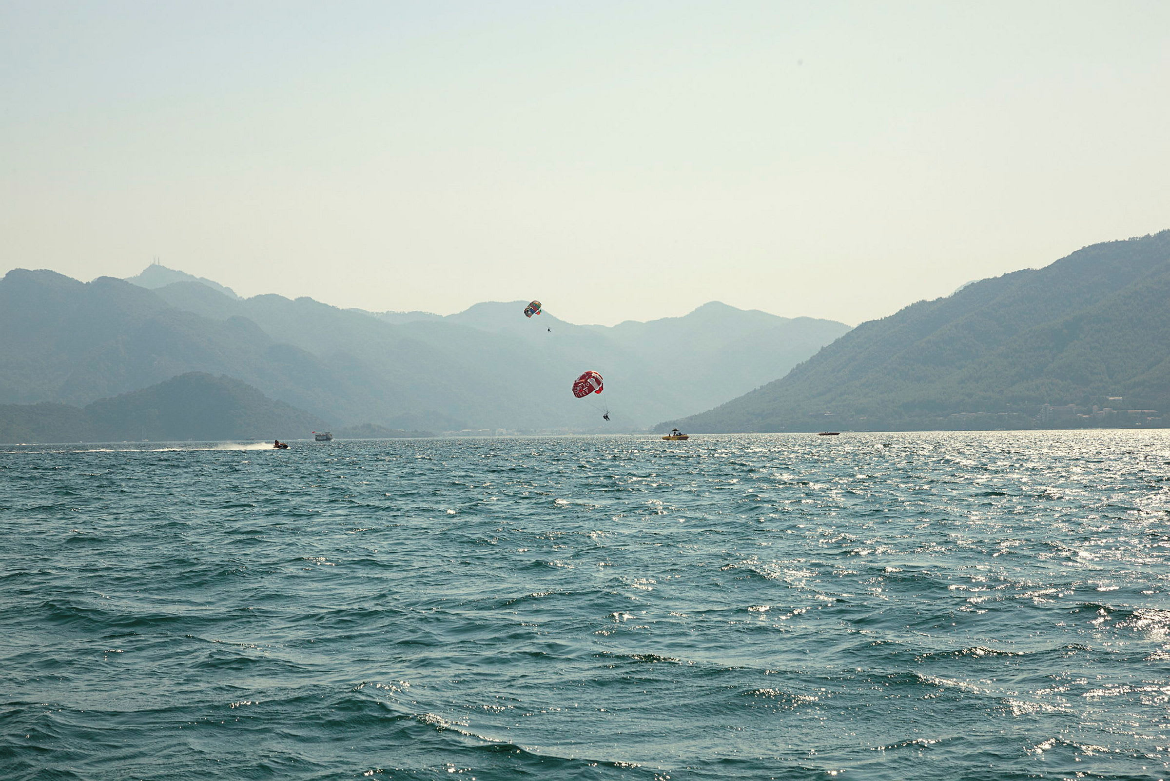 Vy över havet med berg i bakgrunden och personer som ägnar sig åt parasailing. (AI-genererad text)
