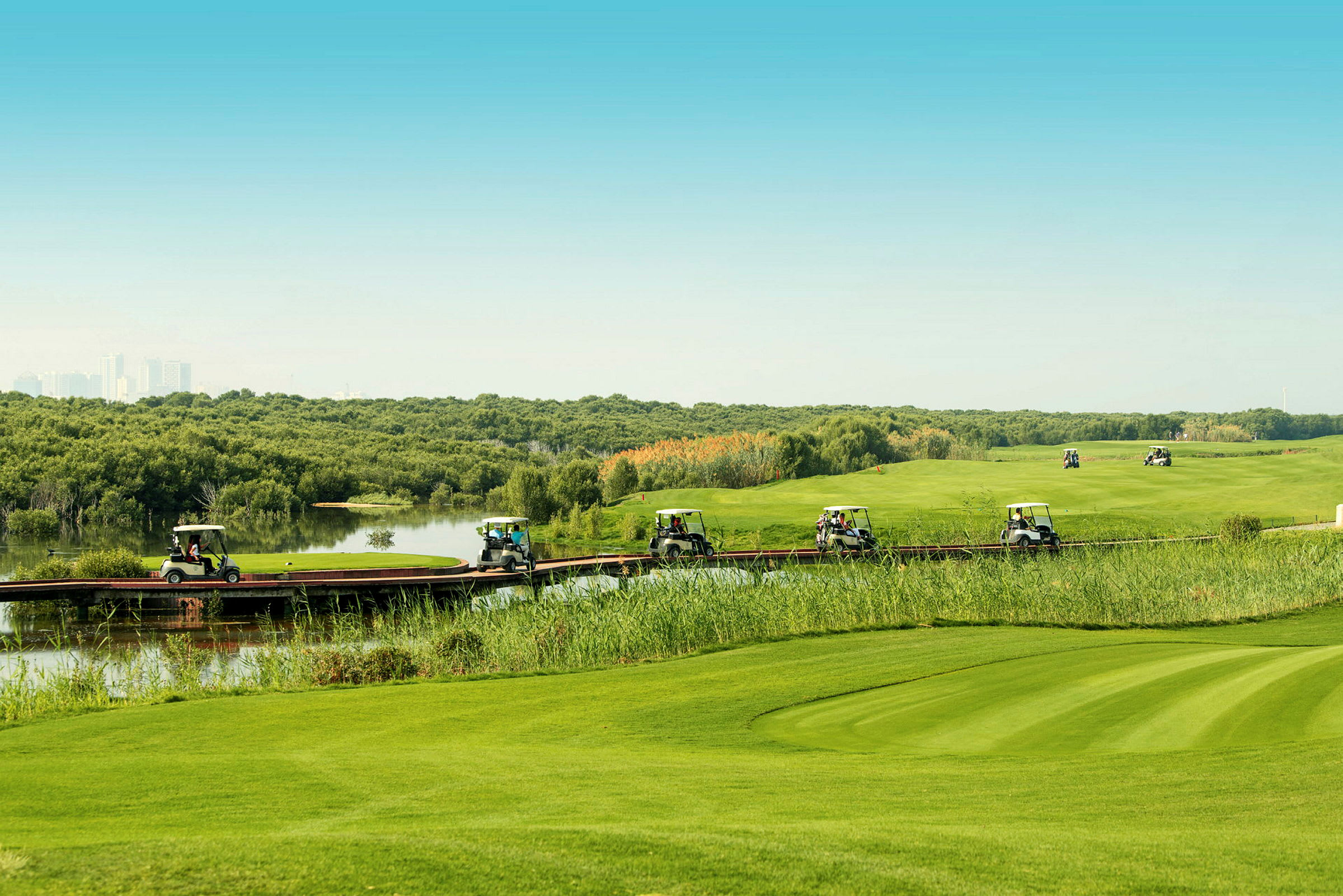 Flera golfbilar kör på en smal träbro som går genom ett grönt landskap med vatten och vegetation. (AI-genererad text)