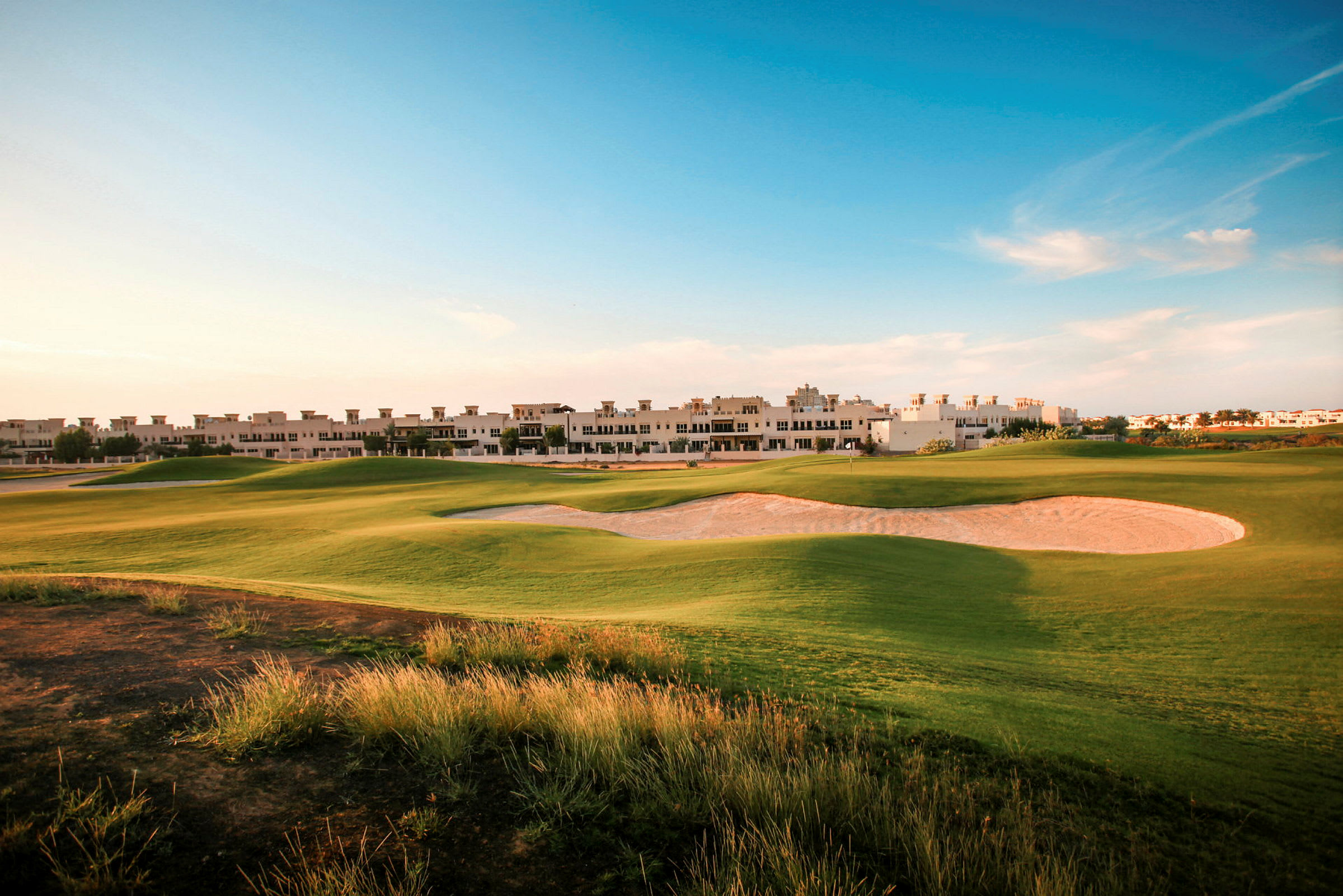 En golfbana med ett sandområde och gröna ytor framför en byggnad. (AI-genererad text)