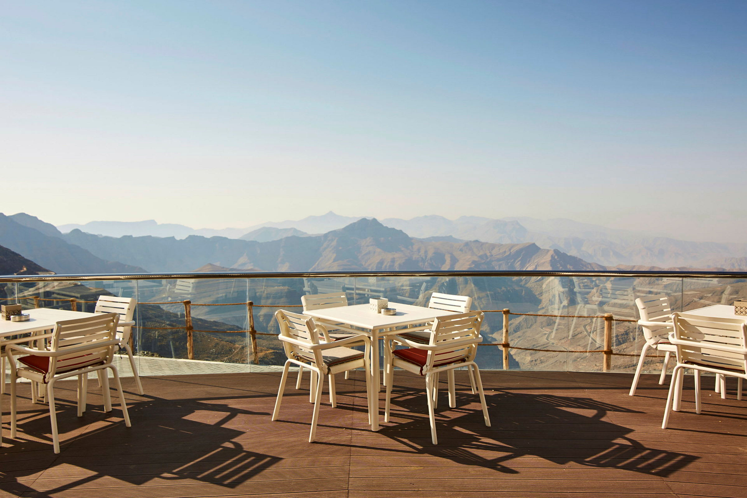 Utsikt över berg från en terrass med vita bord och stolar. (AI-genererad text)