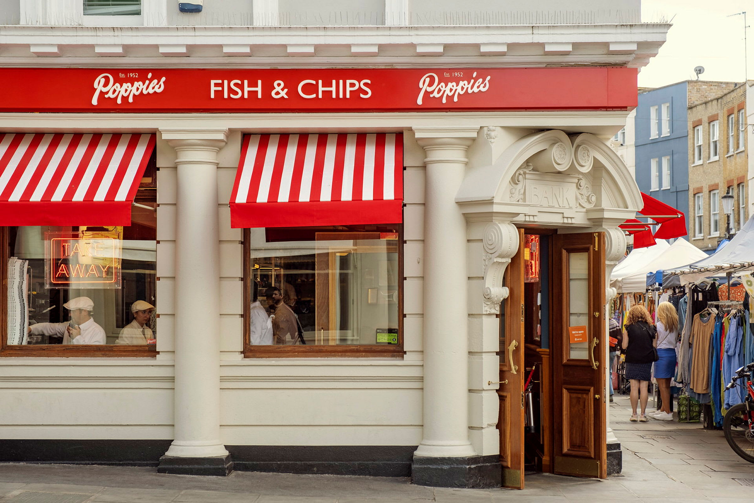 Fasad av en restaurang med röda och vita markiser, skylten 'Fish & Chips', och öppna dörrar. (AI-genererad text)