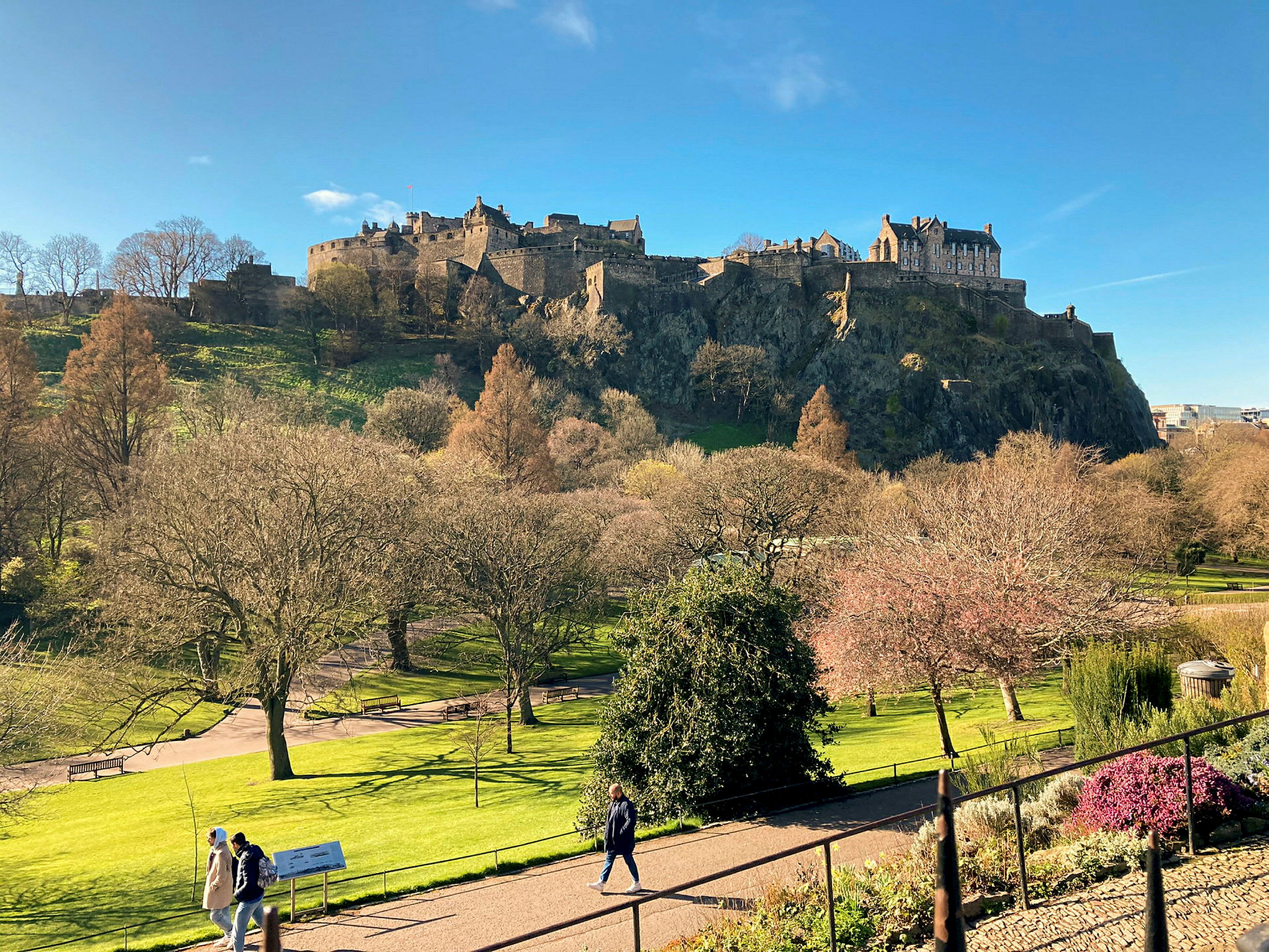 Utsikt över Edinburgh Castle på en solig dag, omgivet av träd och grönska. (AI-genererad text)