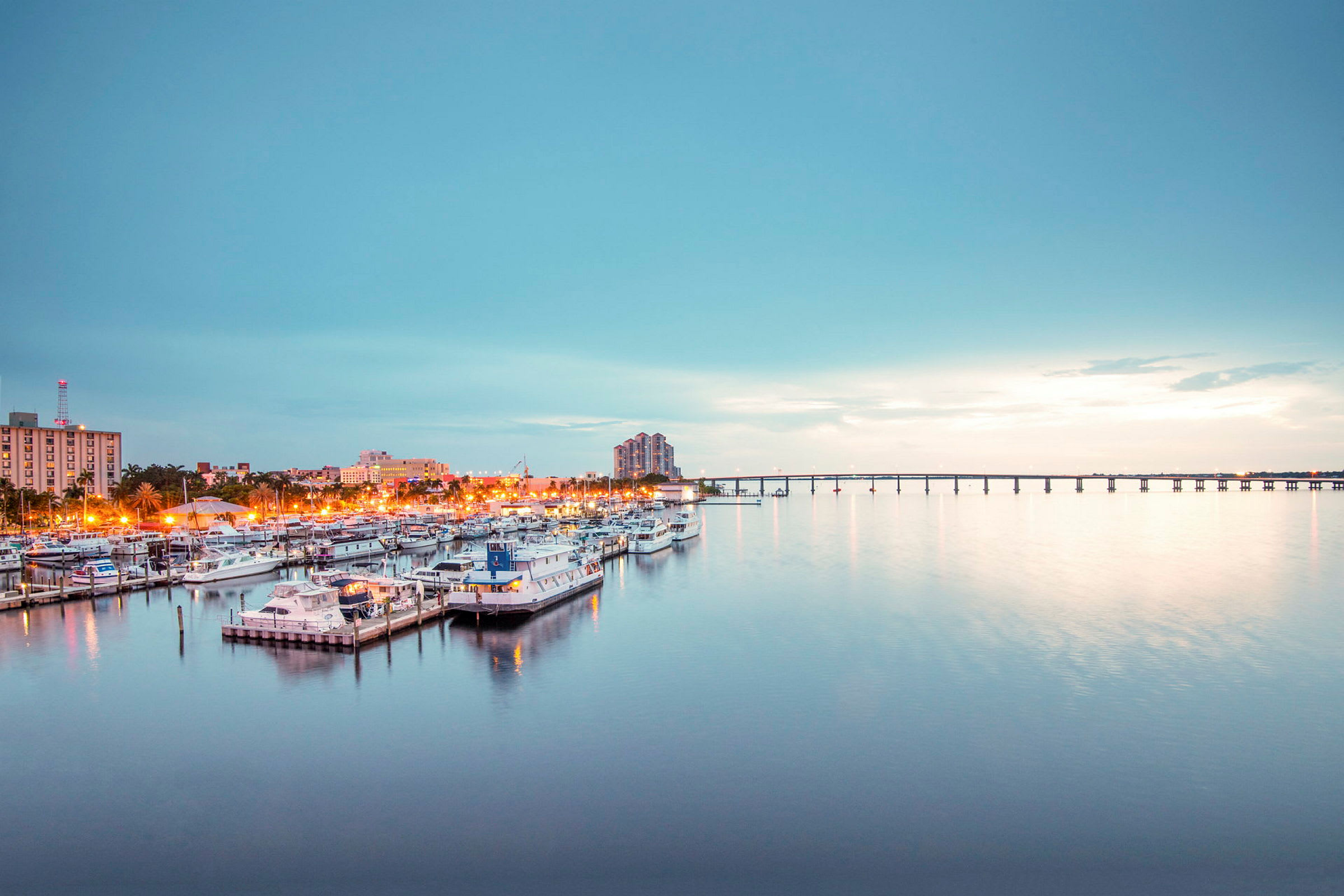 En småbåtshamn med flera båtar, en stad och en bro i bakgrunden. (AI-genererad text)