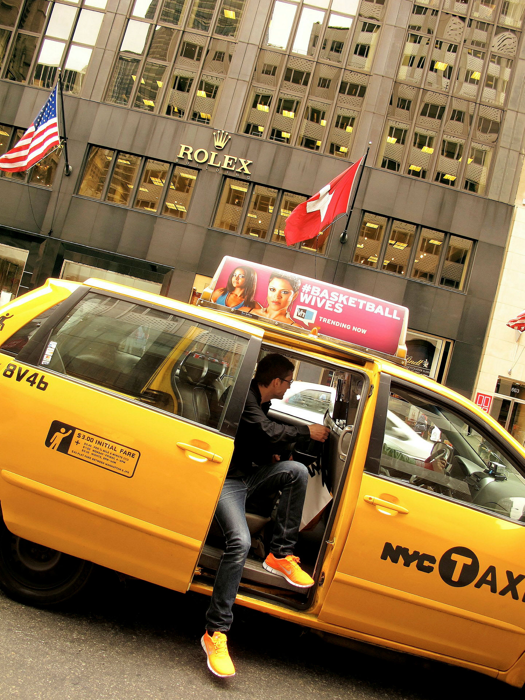 En gul taxi parkerad framför en byggnad med Rolex-logotypen och två flaggor, den amerikanska och den schweiziska. (AI-genererad text)