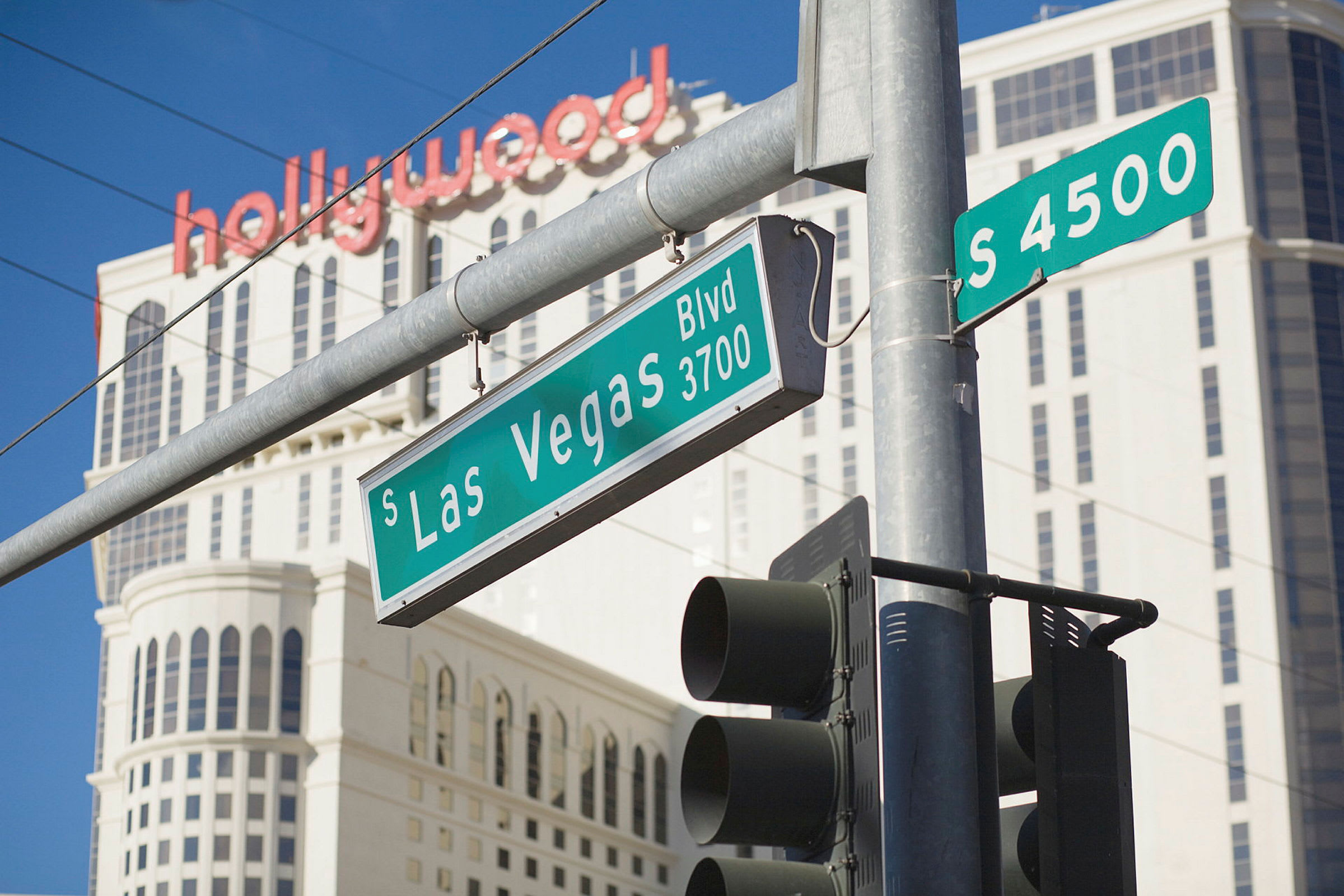 Övergångsställe med trafikljus och gatuskyltar vid South Las Vegas Boulevard, med en hög byggnad och texten "hollywood" i bakgrunden. (AI-genererad text)