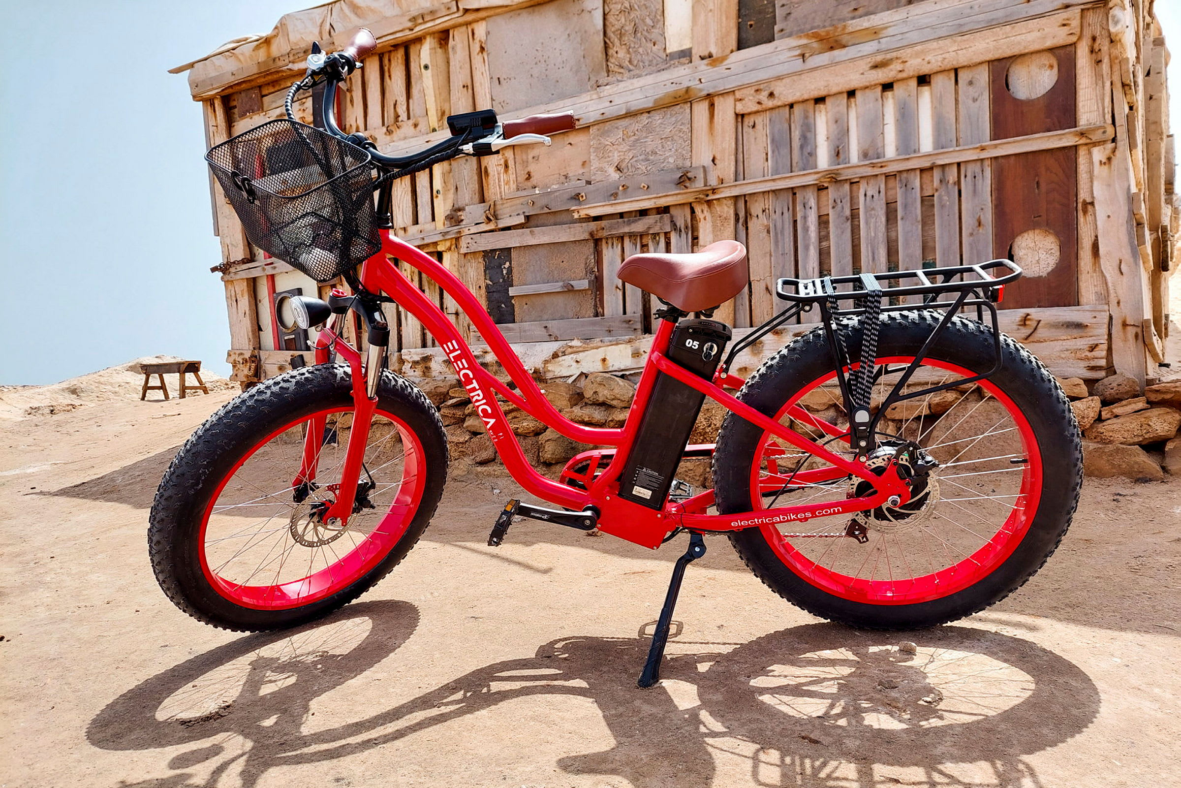 Röd elektrisk cykel står bredvid en träbyggnad i ett ökenlandskap. (AI-genererad text)