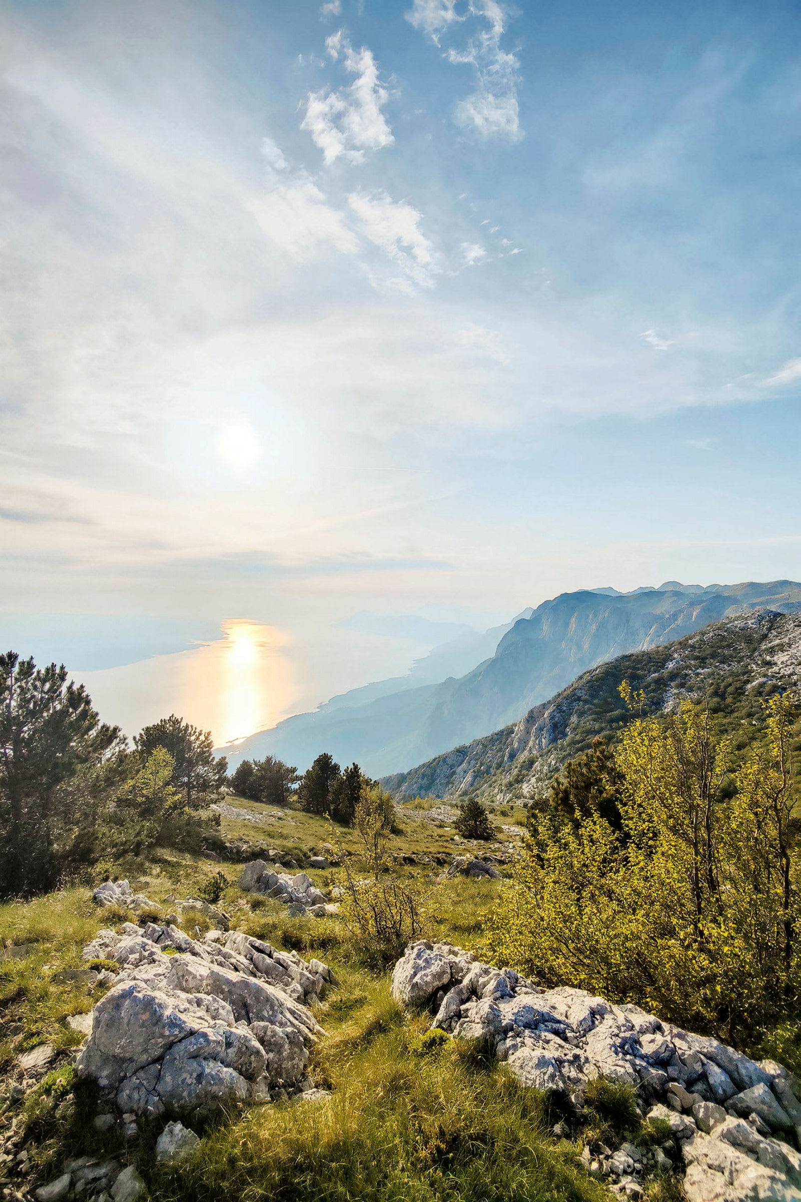Utsikt över ett bergslandskap med grönska, klippor och träd, och havet i bakgrunden vid solnedgång. (AI-genererad text)