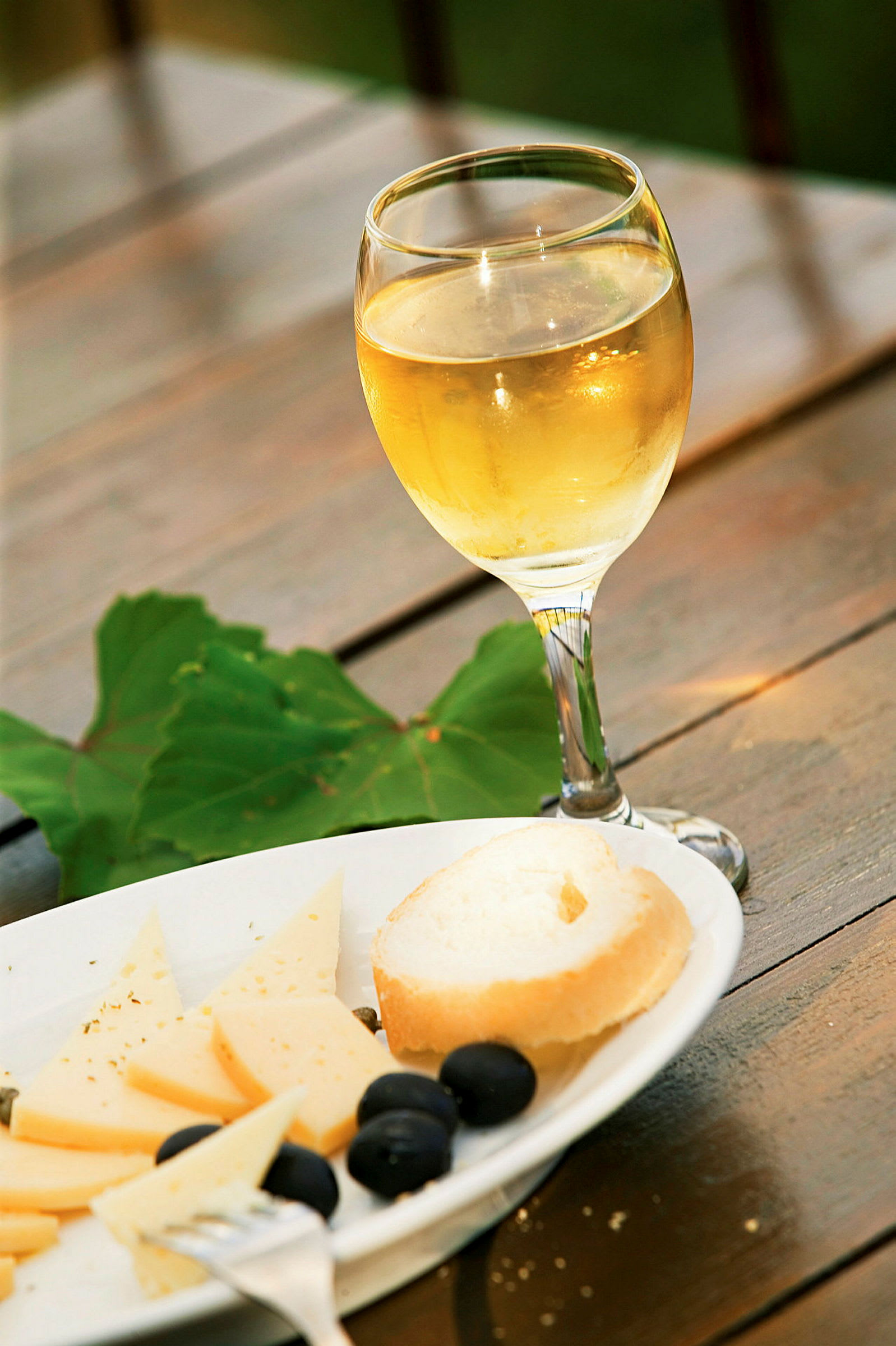 Ett glas vitt vin med bröd, ost och oliver på en tallrik. (AI-genererad text)