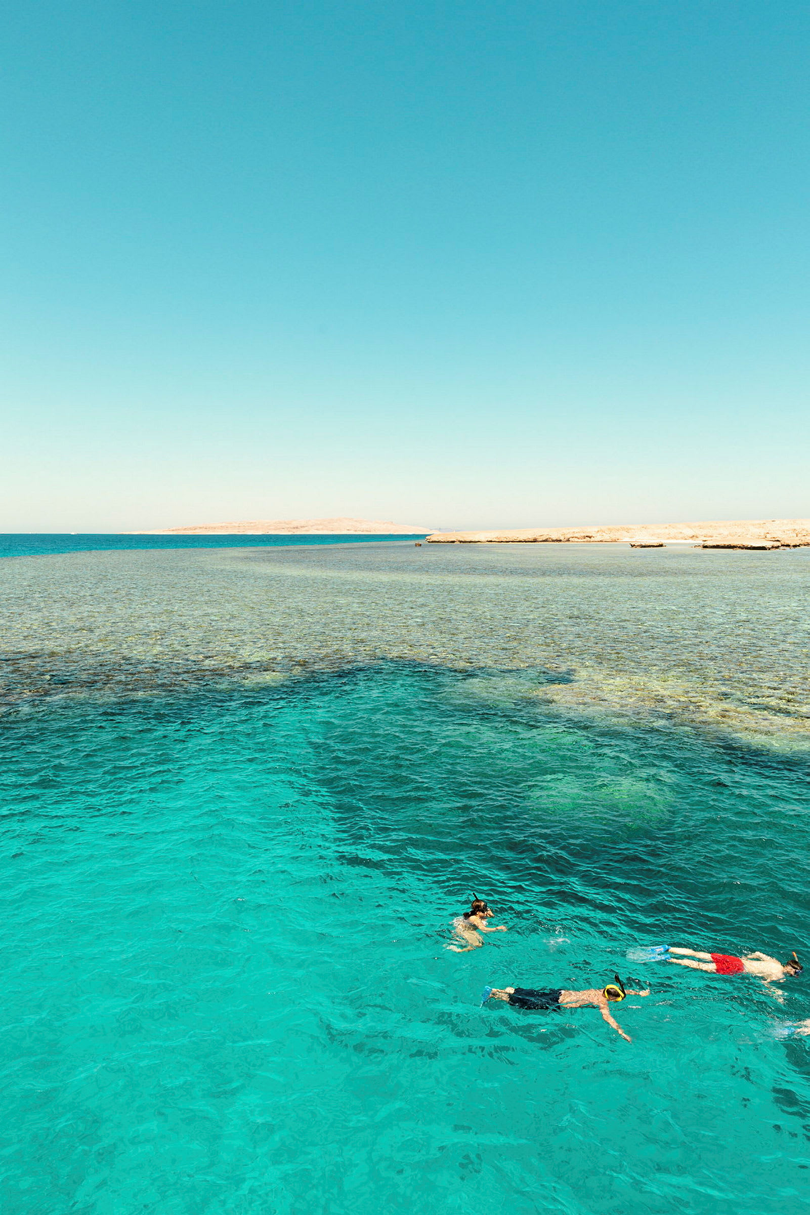 Bilden visar tre personer som snorklar i klart turkost vatten nära en strand. (AI-genererad text)
