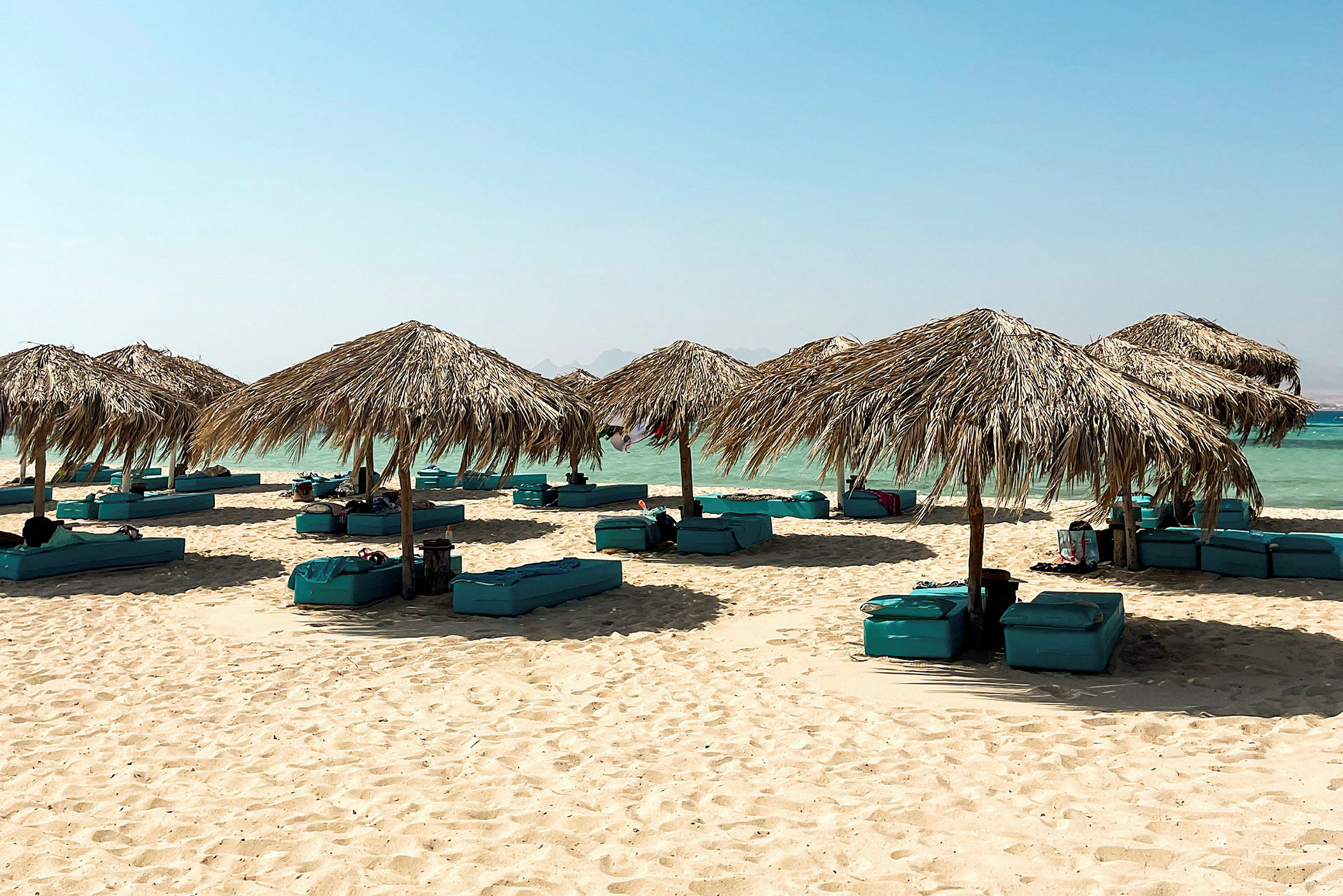 Strand med parasoller av palmblad och solmadrasser på sanden. (AI-genererad text)