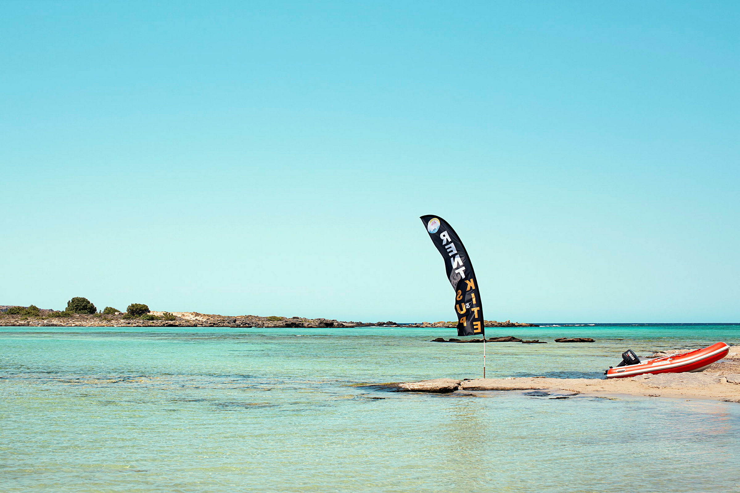 En strand med en flagga och en röd uppblåsbar båt på sanden. (AI-genererad text)