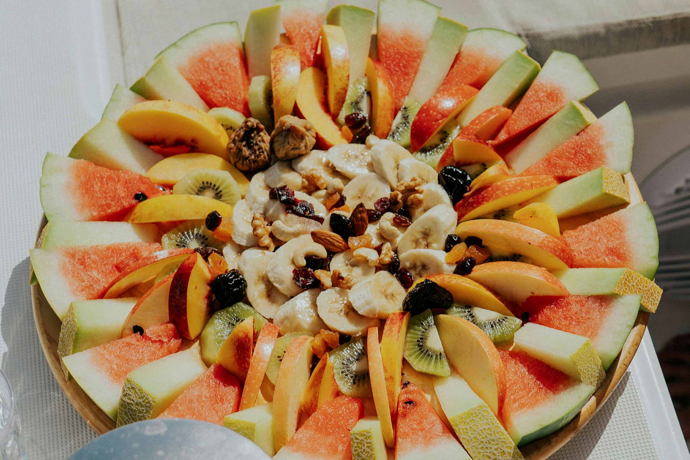 Ett fat med färsk frukt, inklusive melon, kiwi, banan, persika, äppelklyftor och nötter. (AI-genererad text)