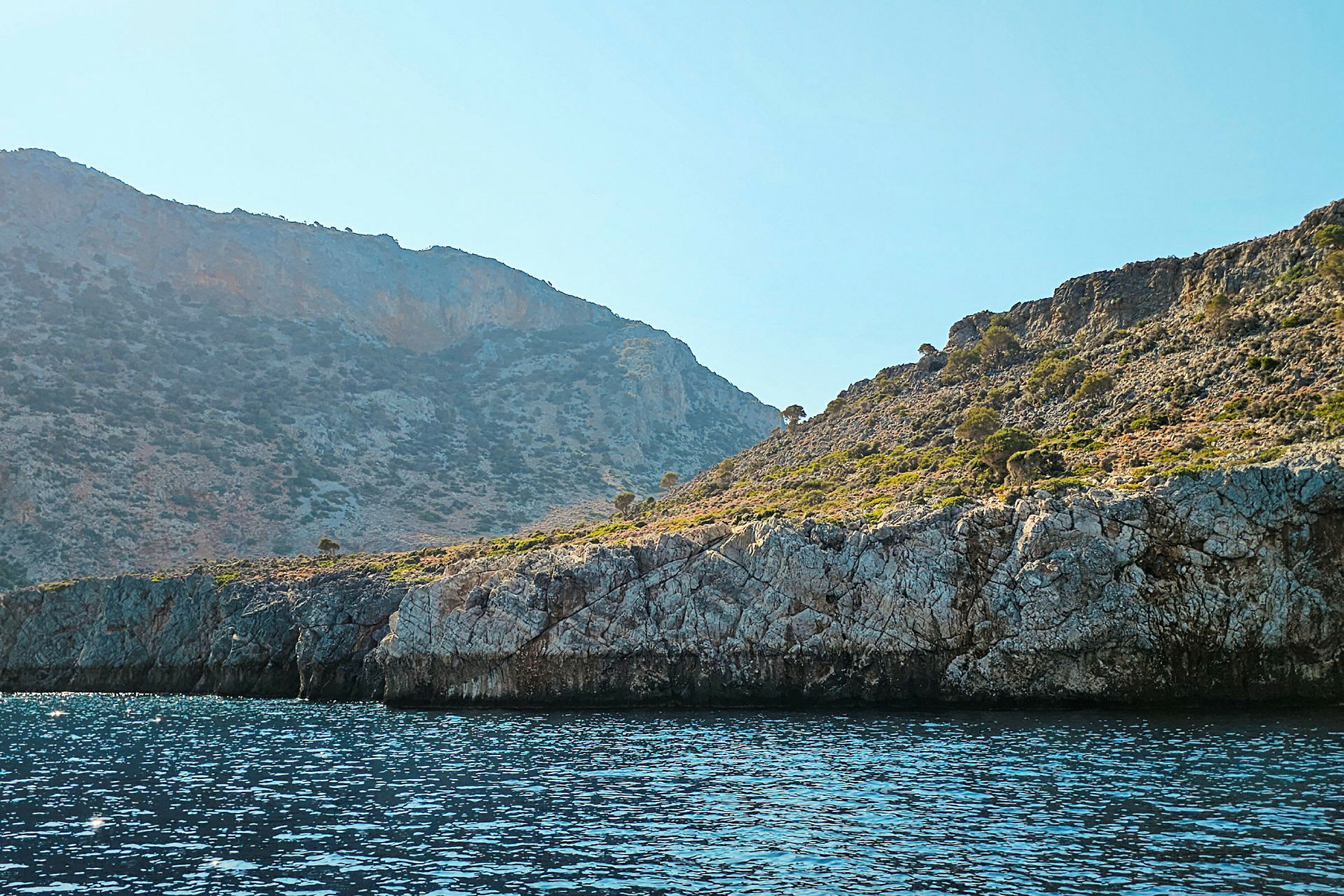 En klippig kustlinje med havet i förgrunden och berg med vegetation i bakgrunden. (AI-genererad text)