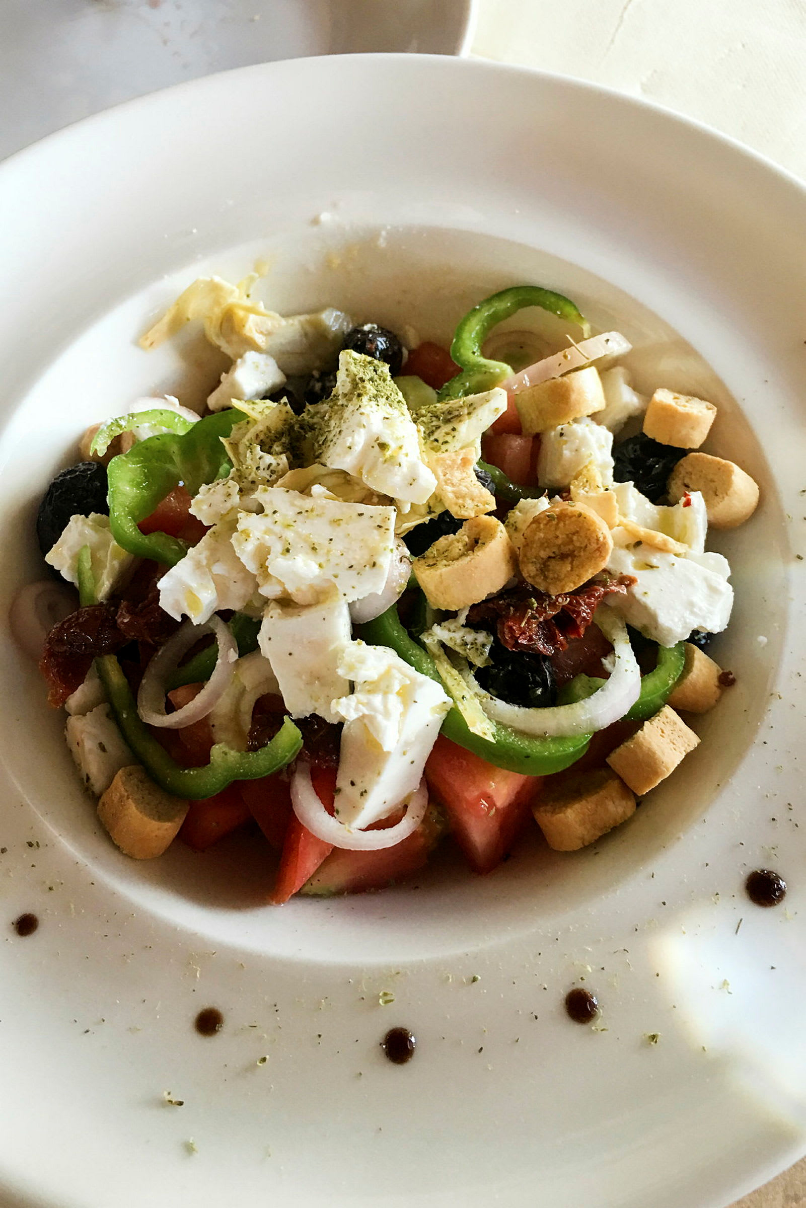 En tallrik med sallad, innehållande tomat, paprika, lök, fetaost, oliver och krutonger. (AI-genererad text)