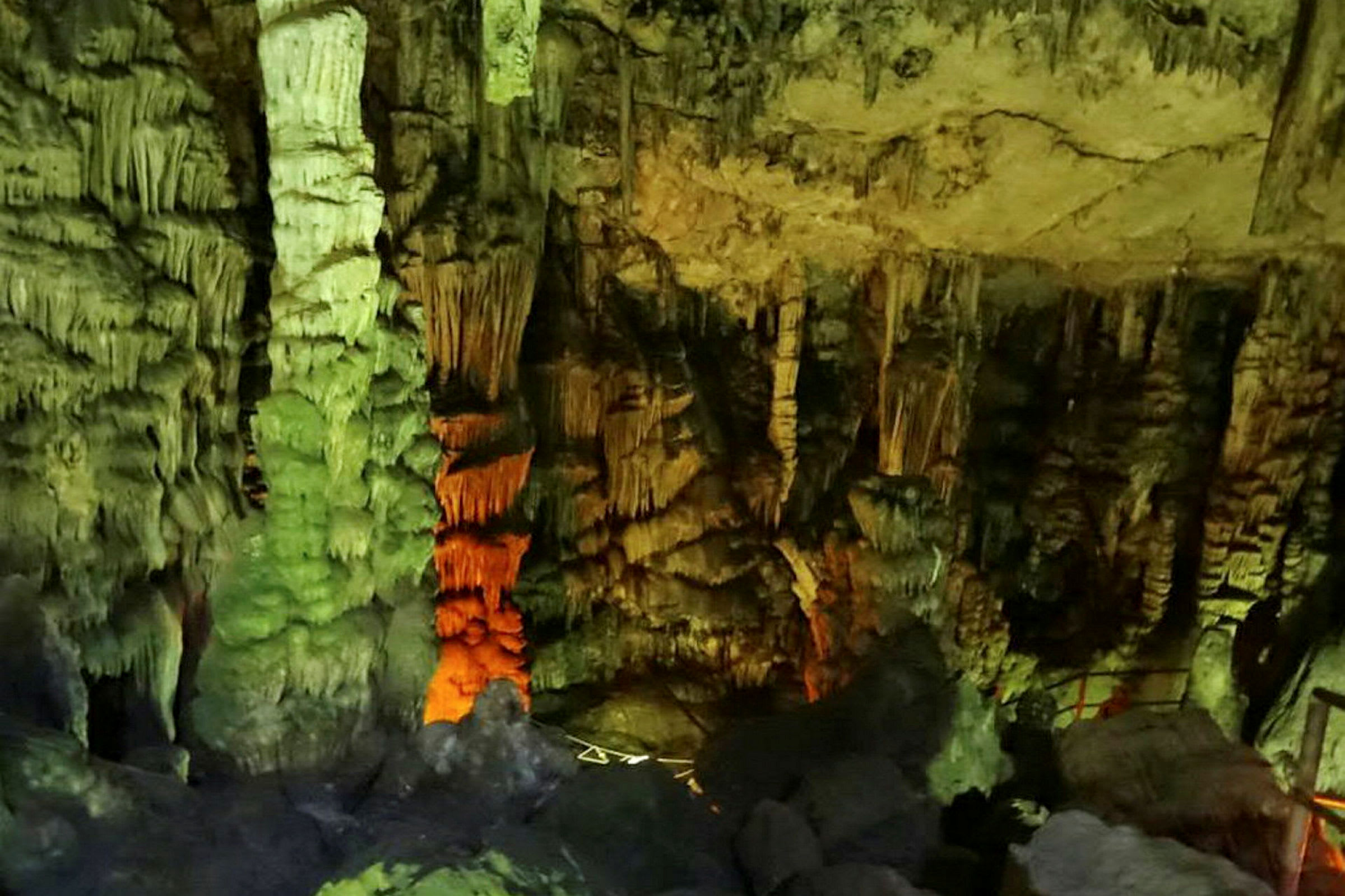 Bild av en grotta med stalaktiter och stalagmiter, belyst med olika färger. (AI-genererad text)