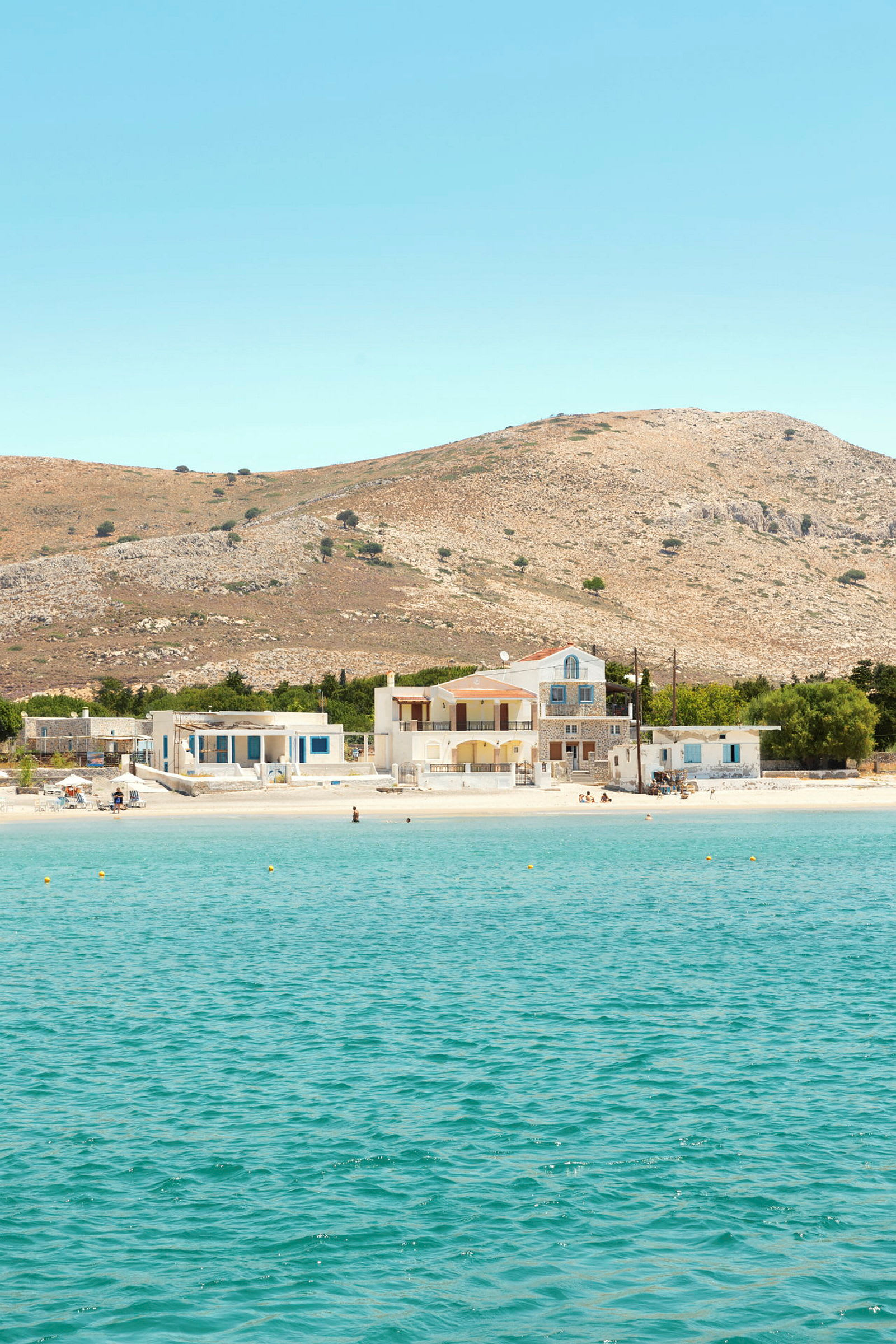 Bild av en klarblå havsvik med en sandstrand som har hus och kullar i bakgrunden. (AI-genererad text)