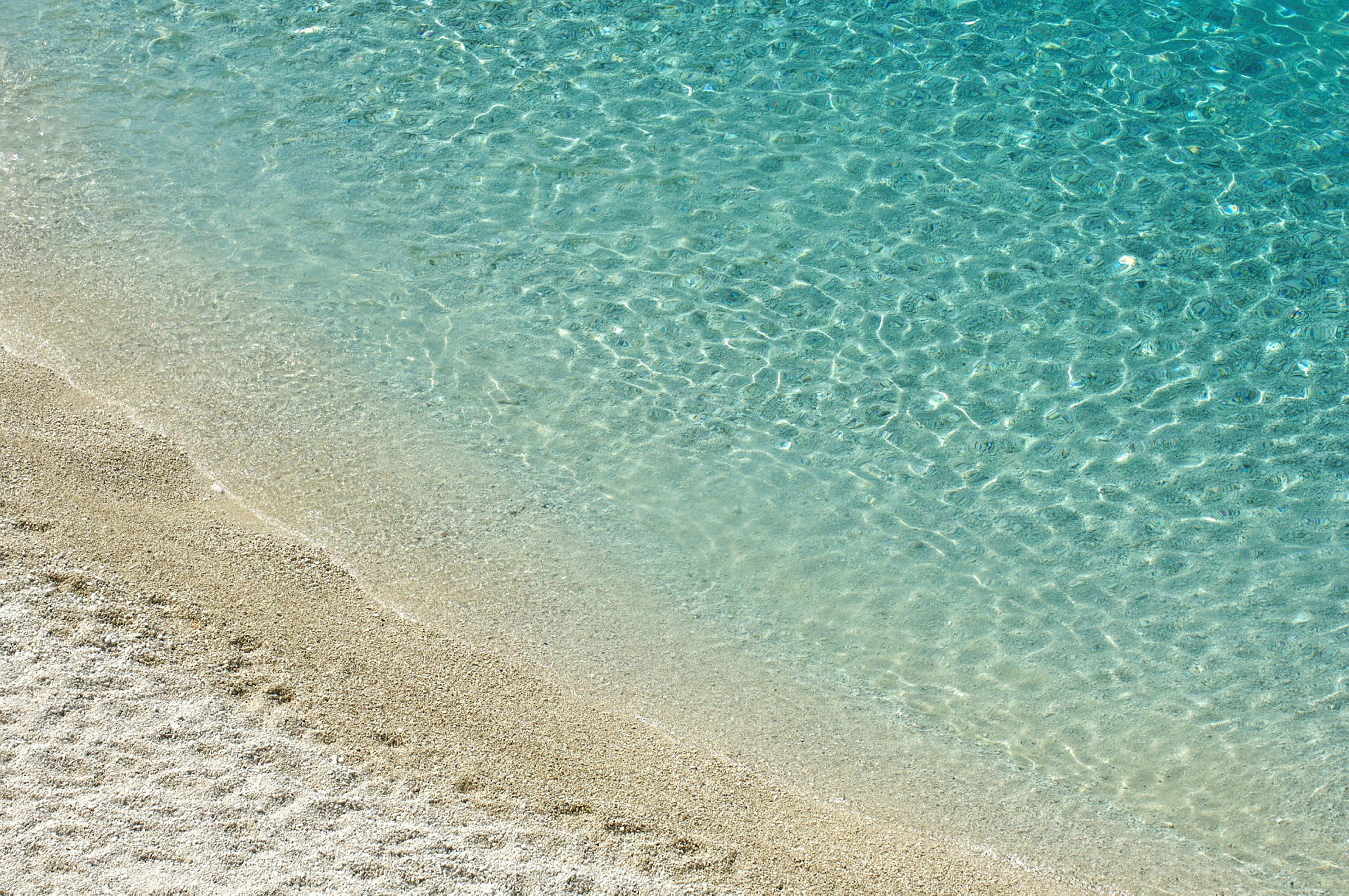 Vyn visar en strandkant där klarblått vatten möter ljus sand. (AI-genererad text)