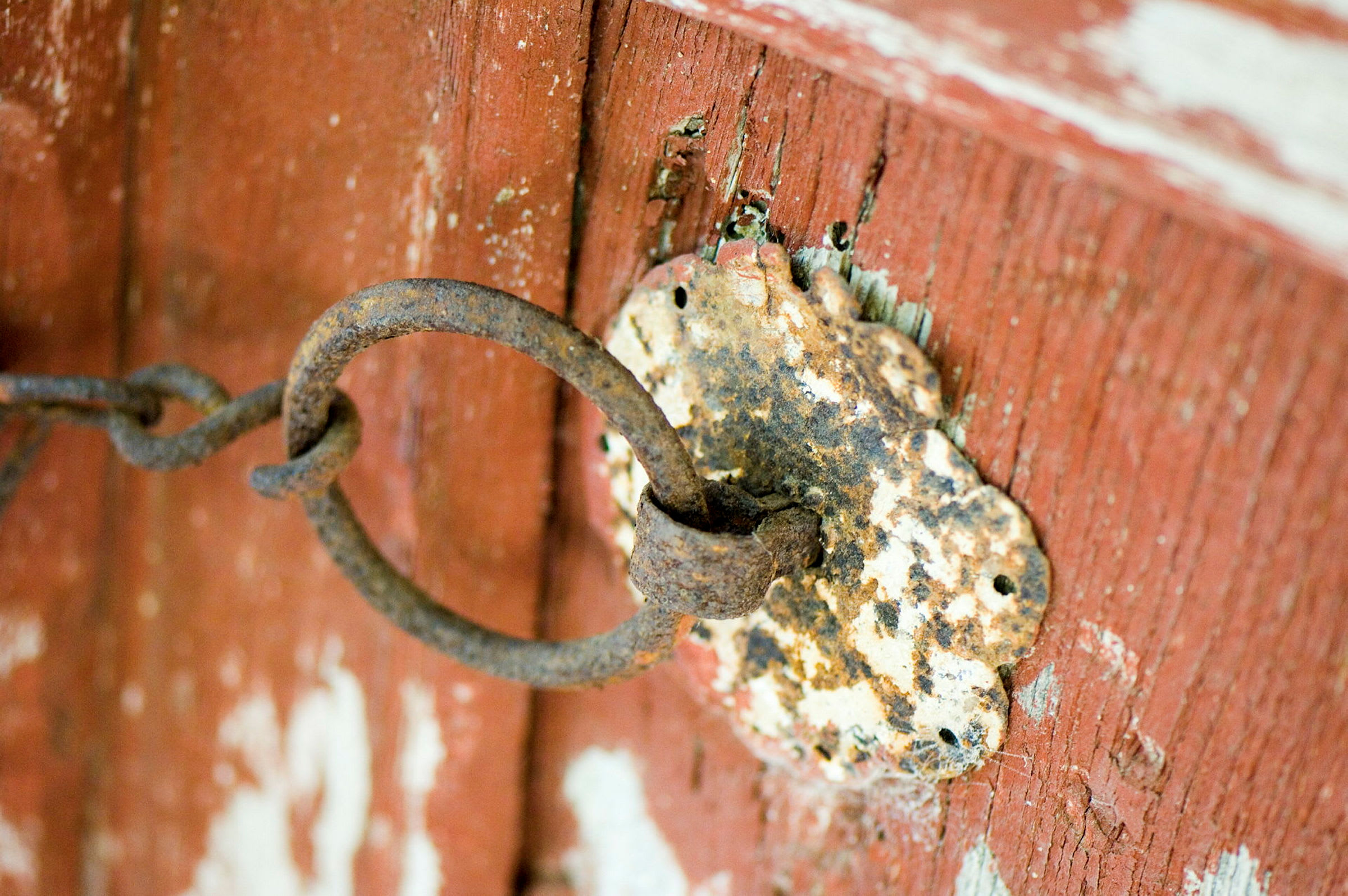 Närbild på en rostig metalldetalj och kedja fäst vid en röd träyta. (AI-genererad text)