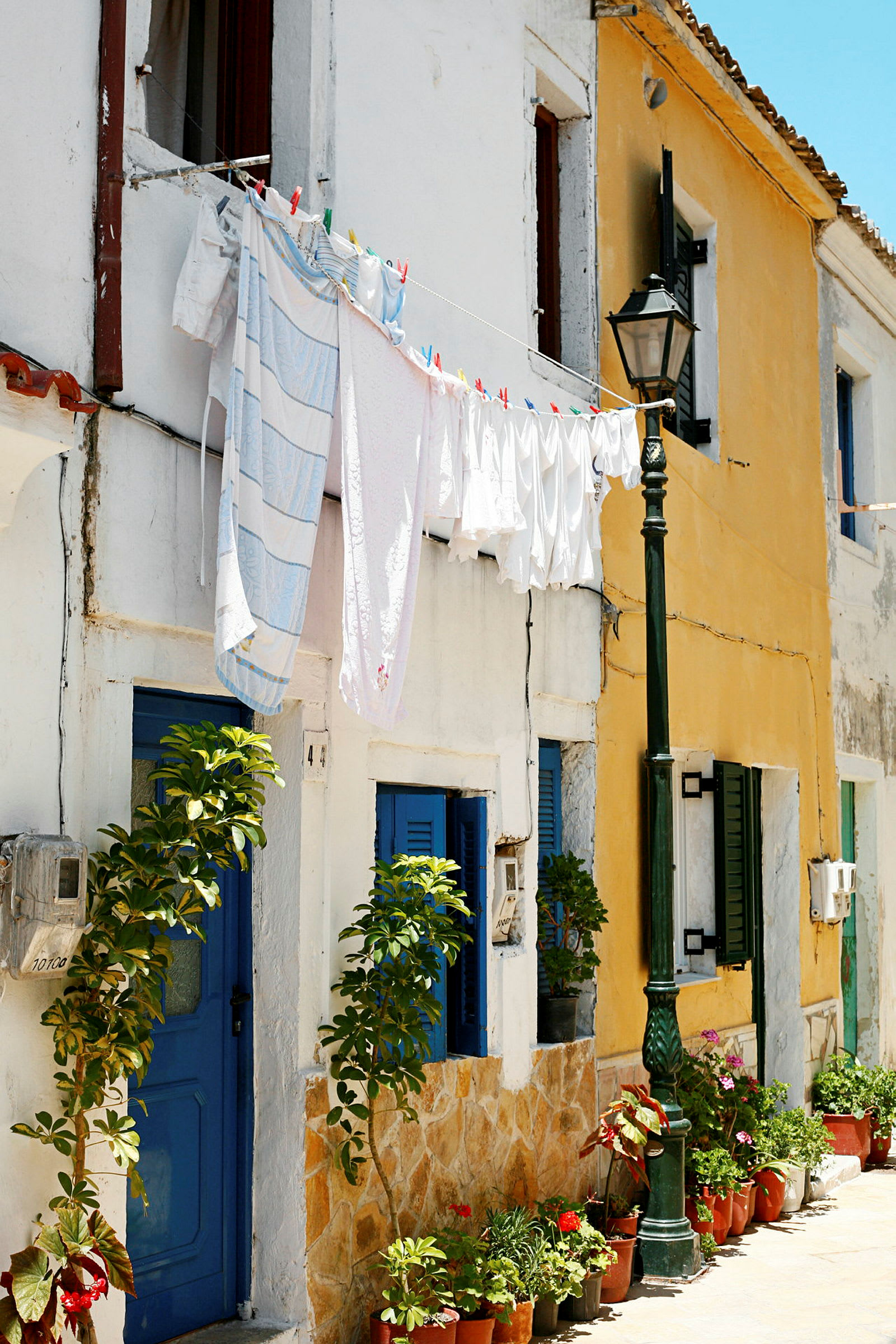 En rad av färgglada hus med blå dörrar och fönsterluckor. Tvätt hänger på en lina mellan husen, och det är blommor i krukor framför dem. (AI-genererad text)