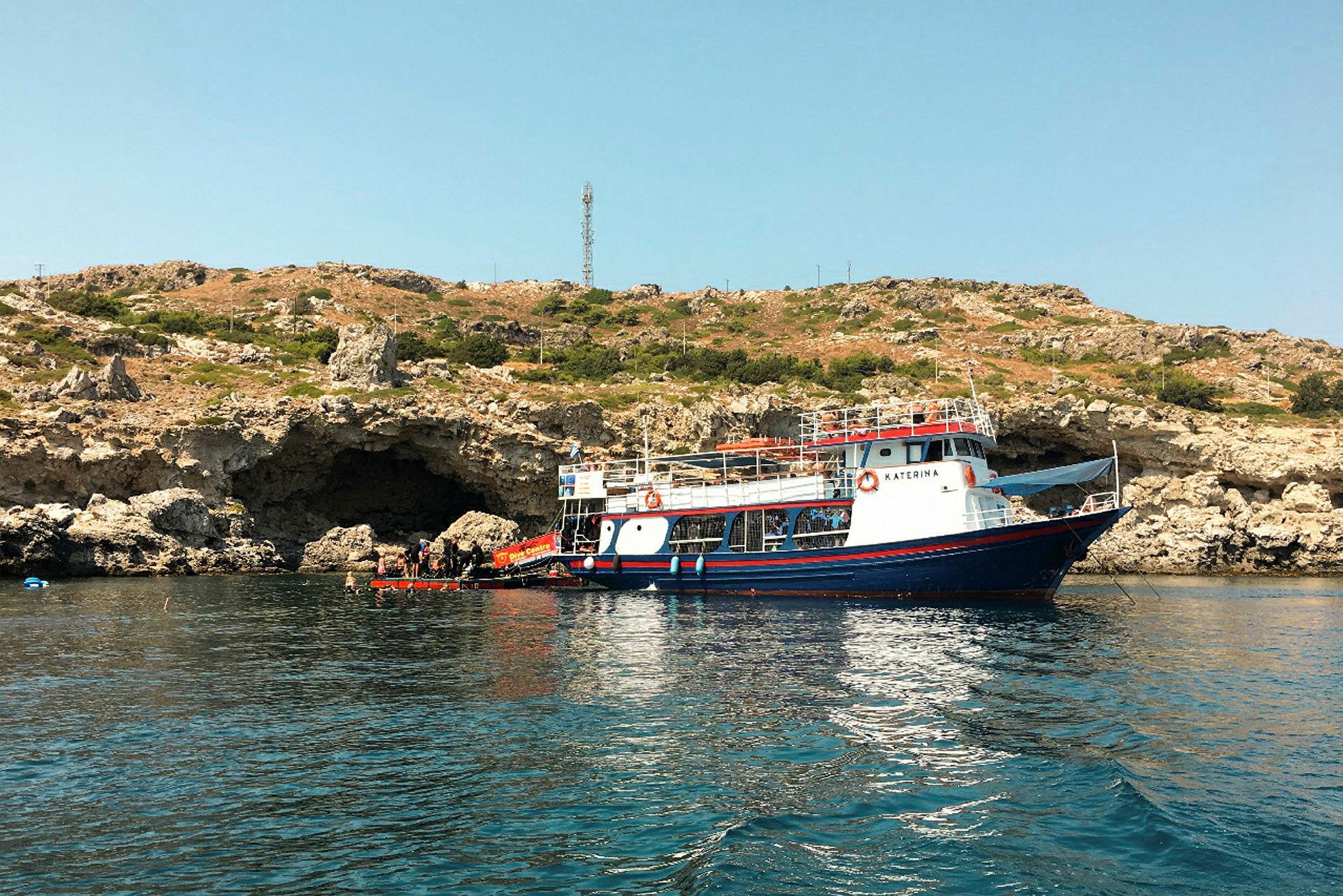 En båt är förtöjd vid en klippig kust med en grotta i bakgrunden. (AI-genererad text)