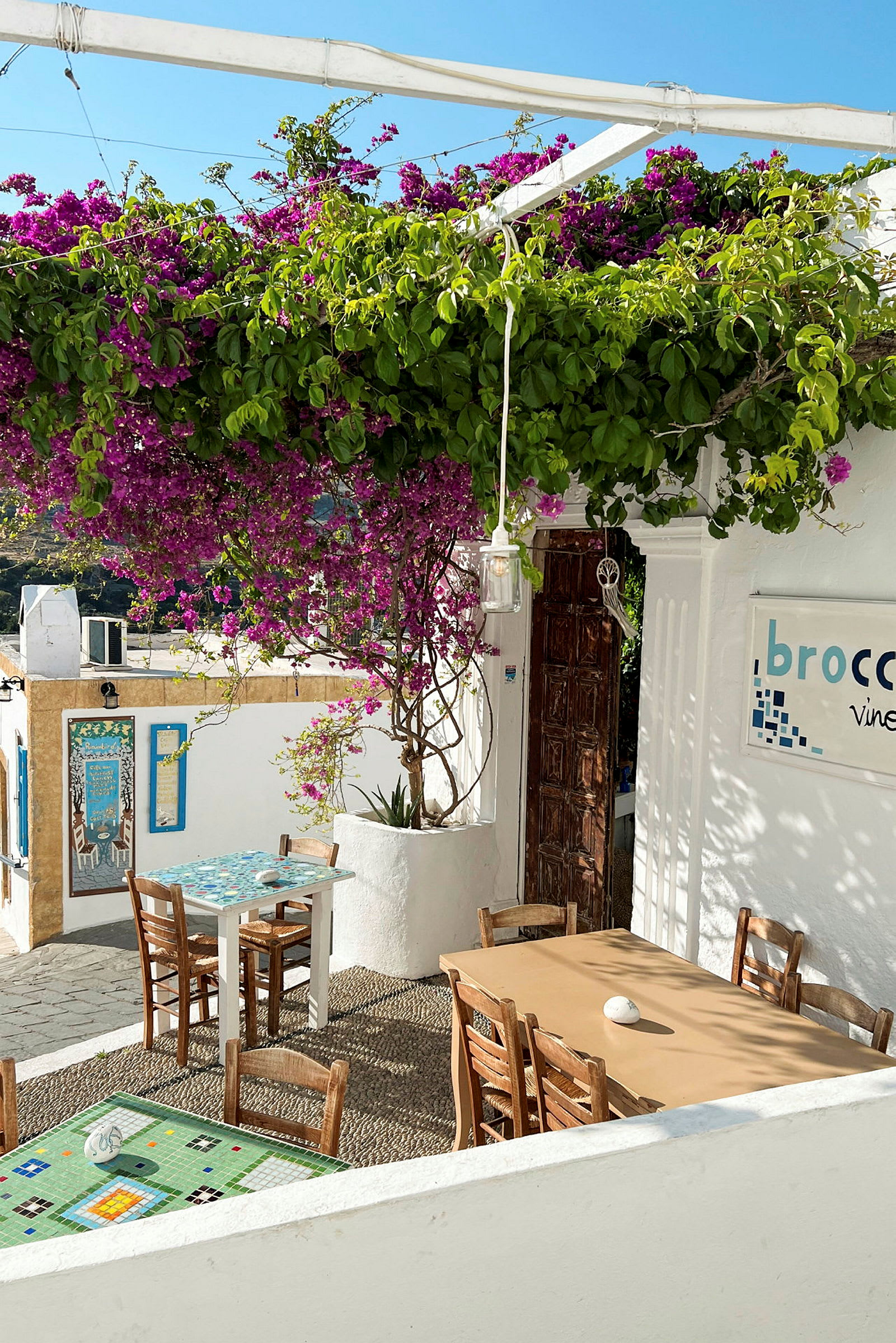 Exteriör av en restaurang med bord och stolar under en blommande pergola. (AI-genererad text)