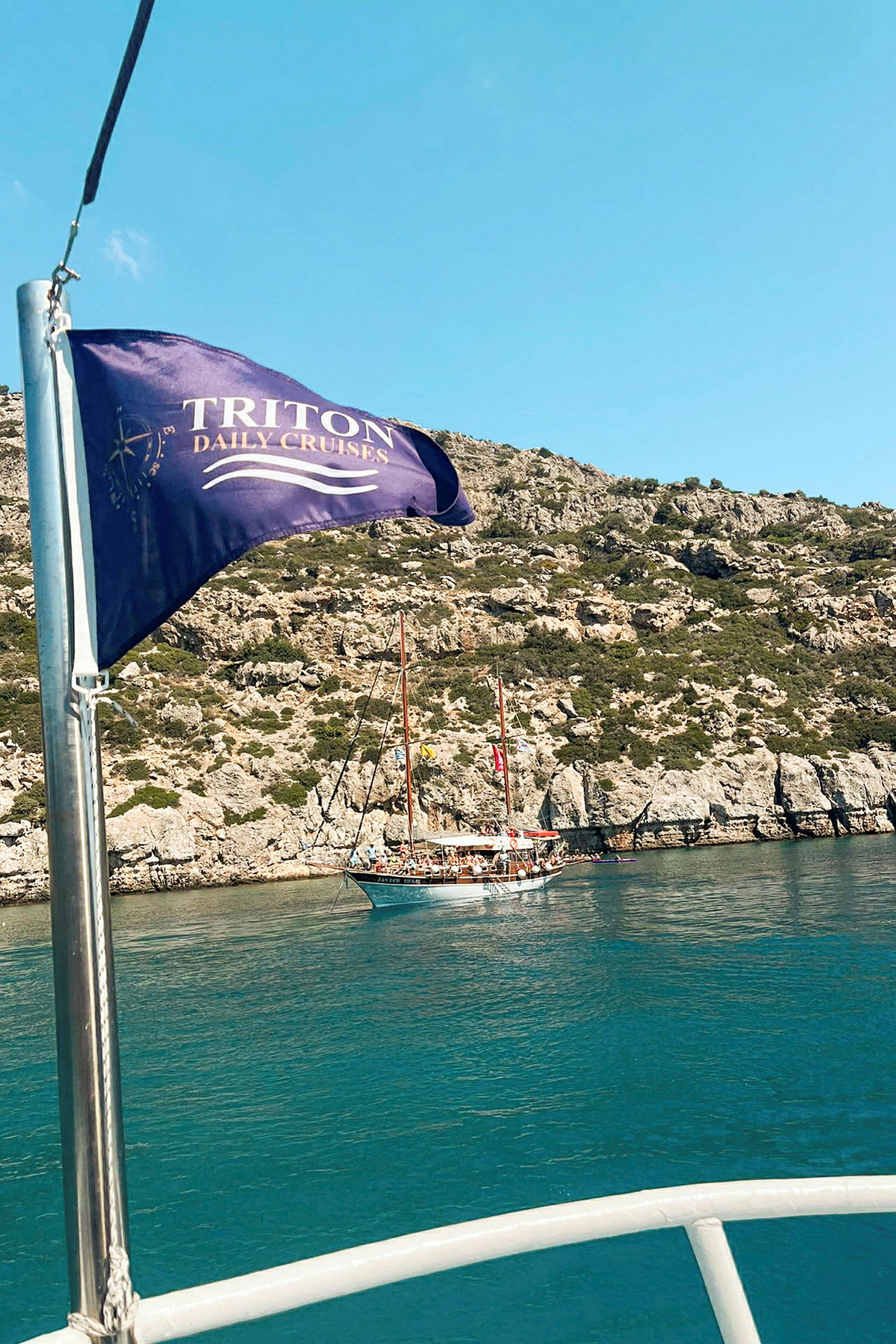 Ett segelfartyg ligger vid en klippa medan en flagga med texten "Triton Daily Cruises" vajar i förgrunden. (AI-genererad text)