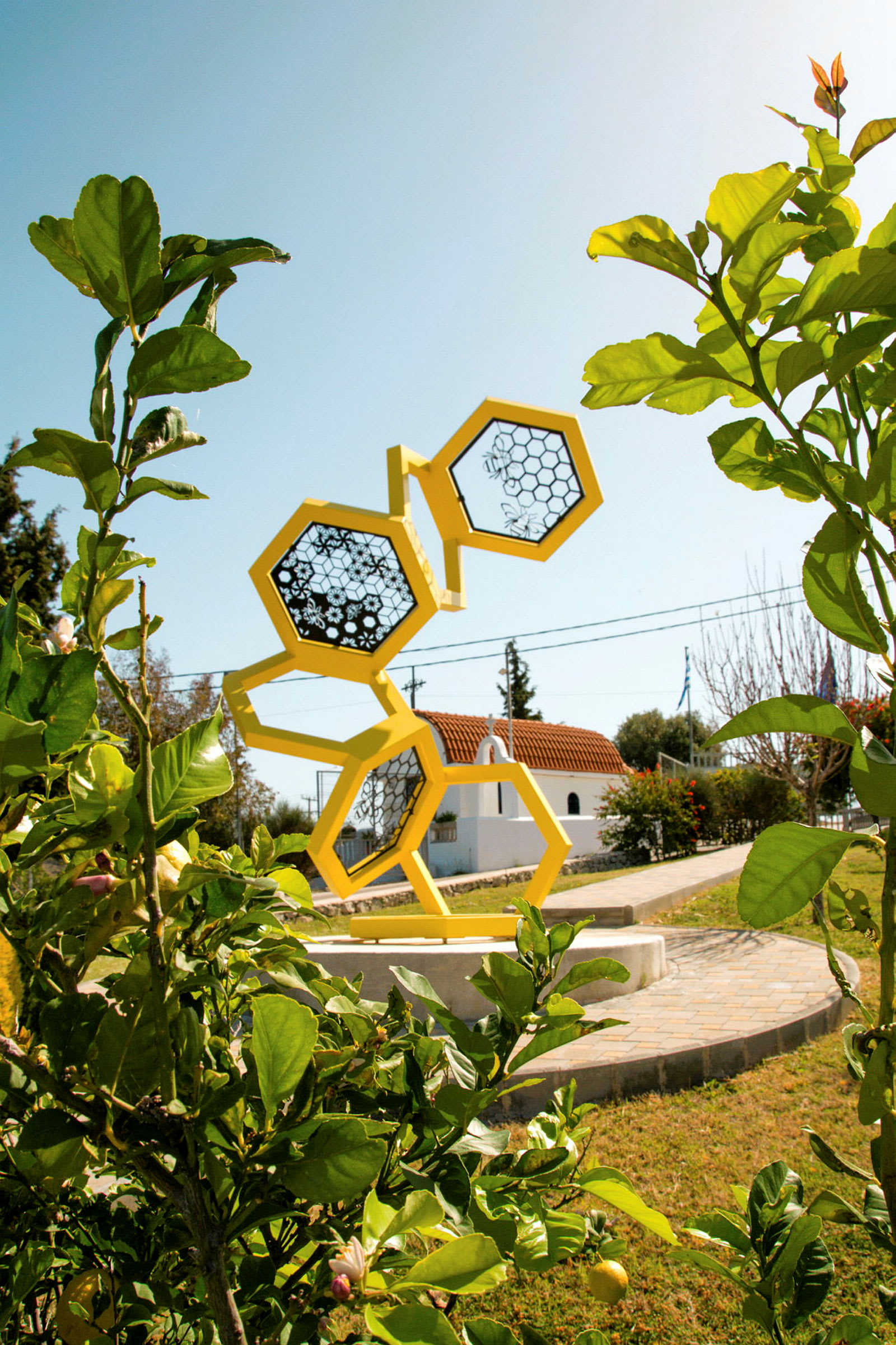 En skulptur av gula hexagoner står i en trädgård med grönska runt omkring. (AI-genererad text)
