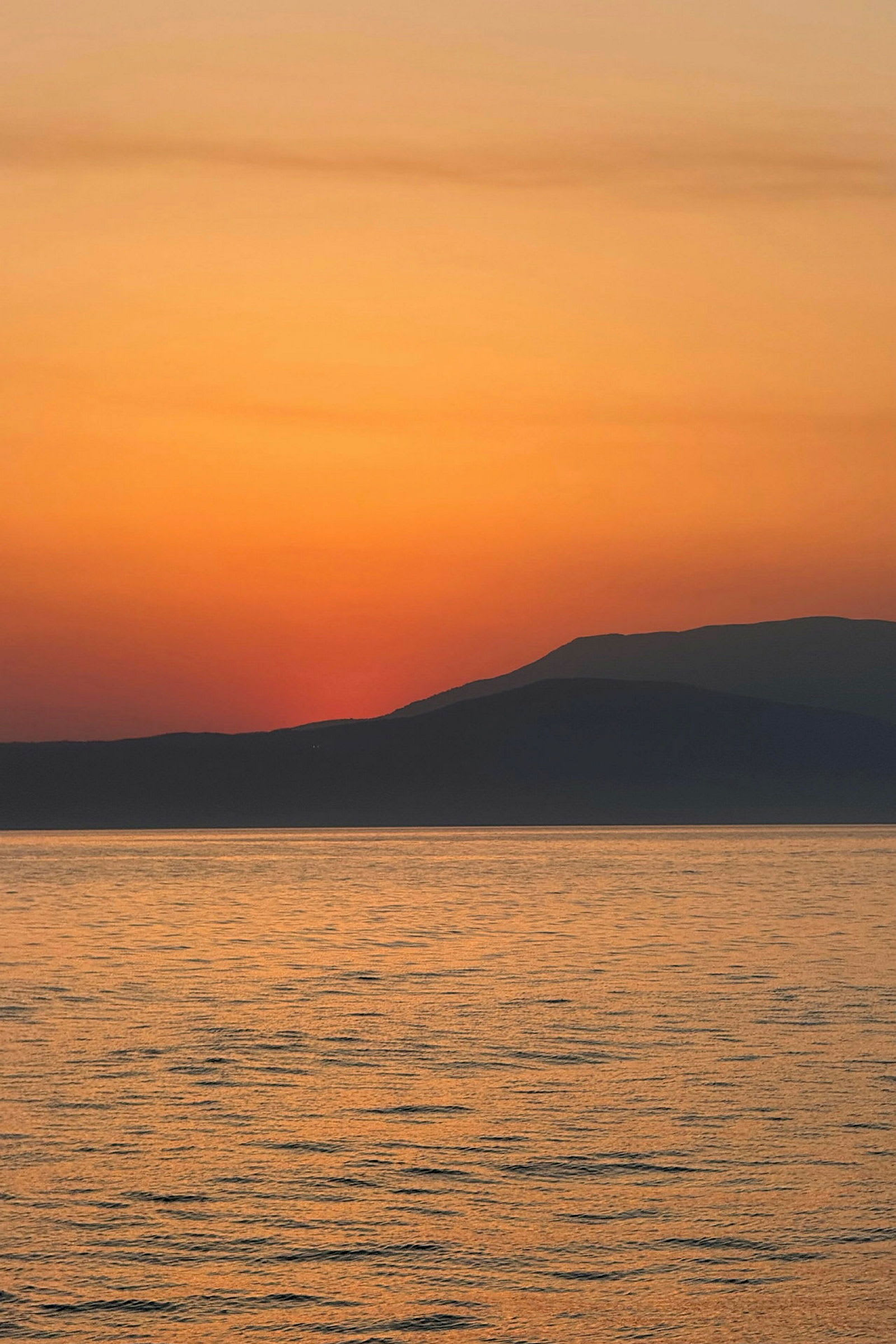 Solnedgång över havet med silhuetter av avlägsna berg. (AI-genererad text)