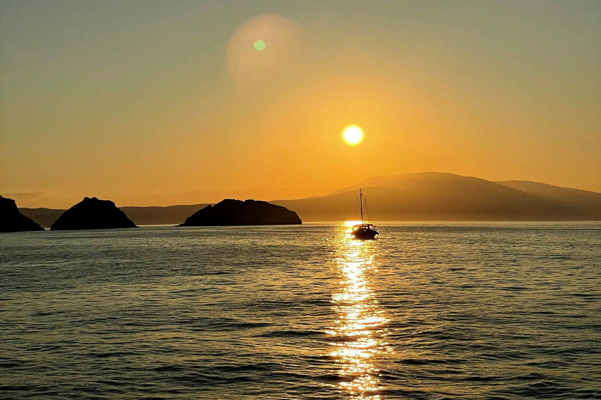 En segelbåt på havet vid solnedgång, med berg i bakgrunden. (AI-genererad text)