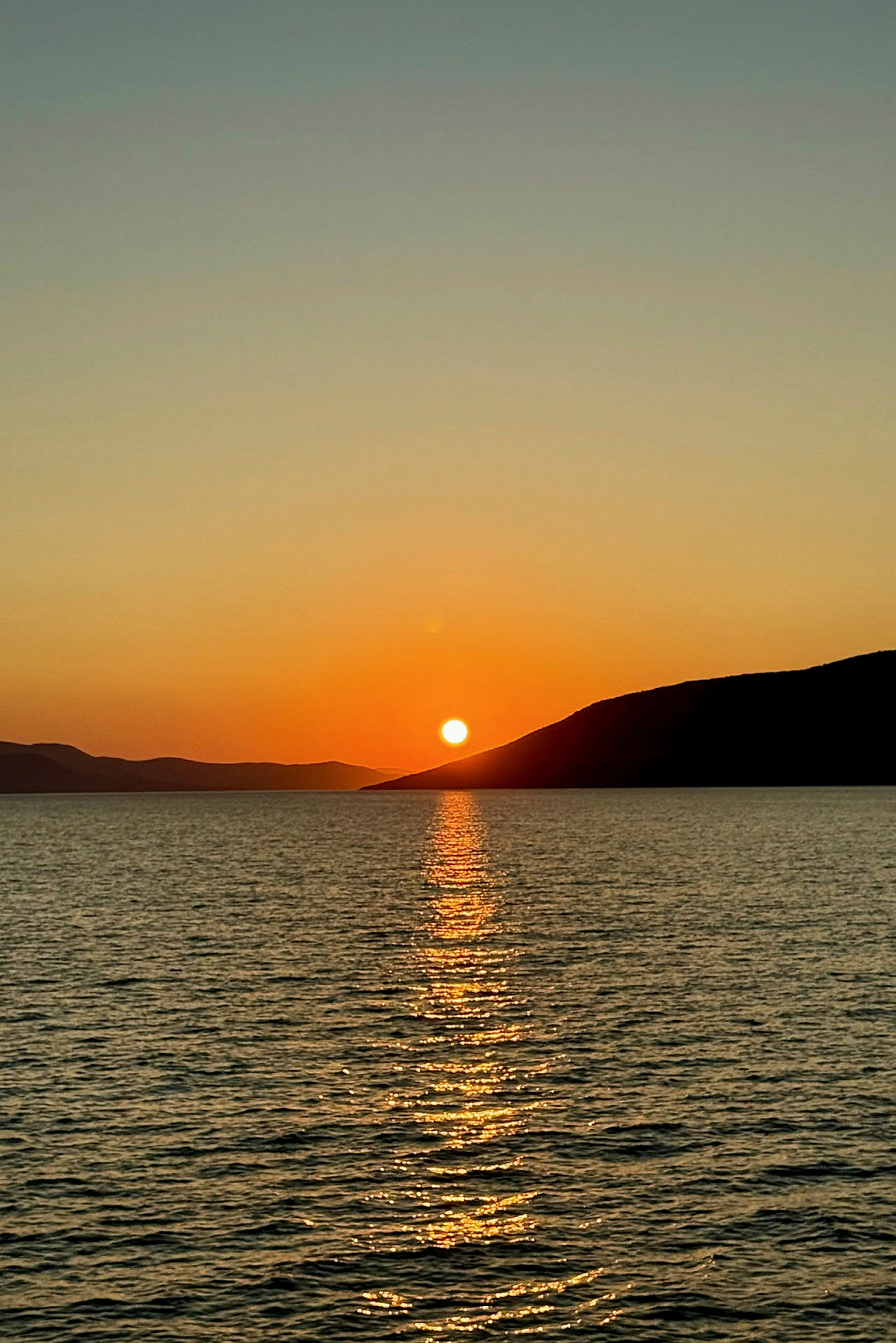 Bild av en solnedgång över havet med speglingar i vattnet och berg i bakgrunden. (AI-genererad text)