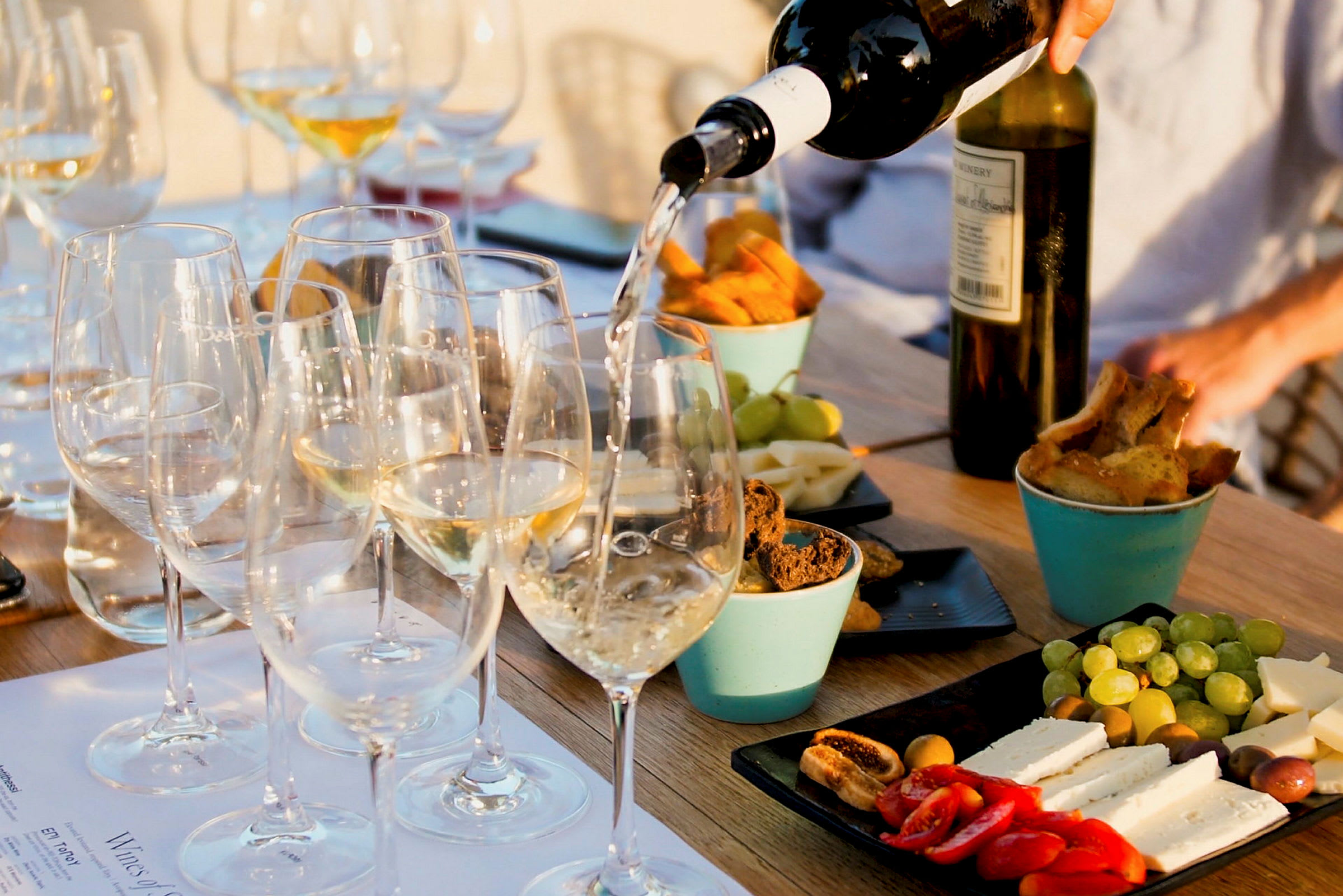 Ett bord med glas fyllda med vitt vin som serveras, omgivna av olika tilltugg som ost, bröd och frukt. (AI-genererad text)
