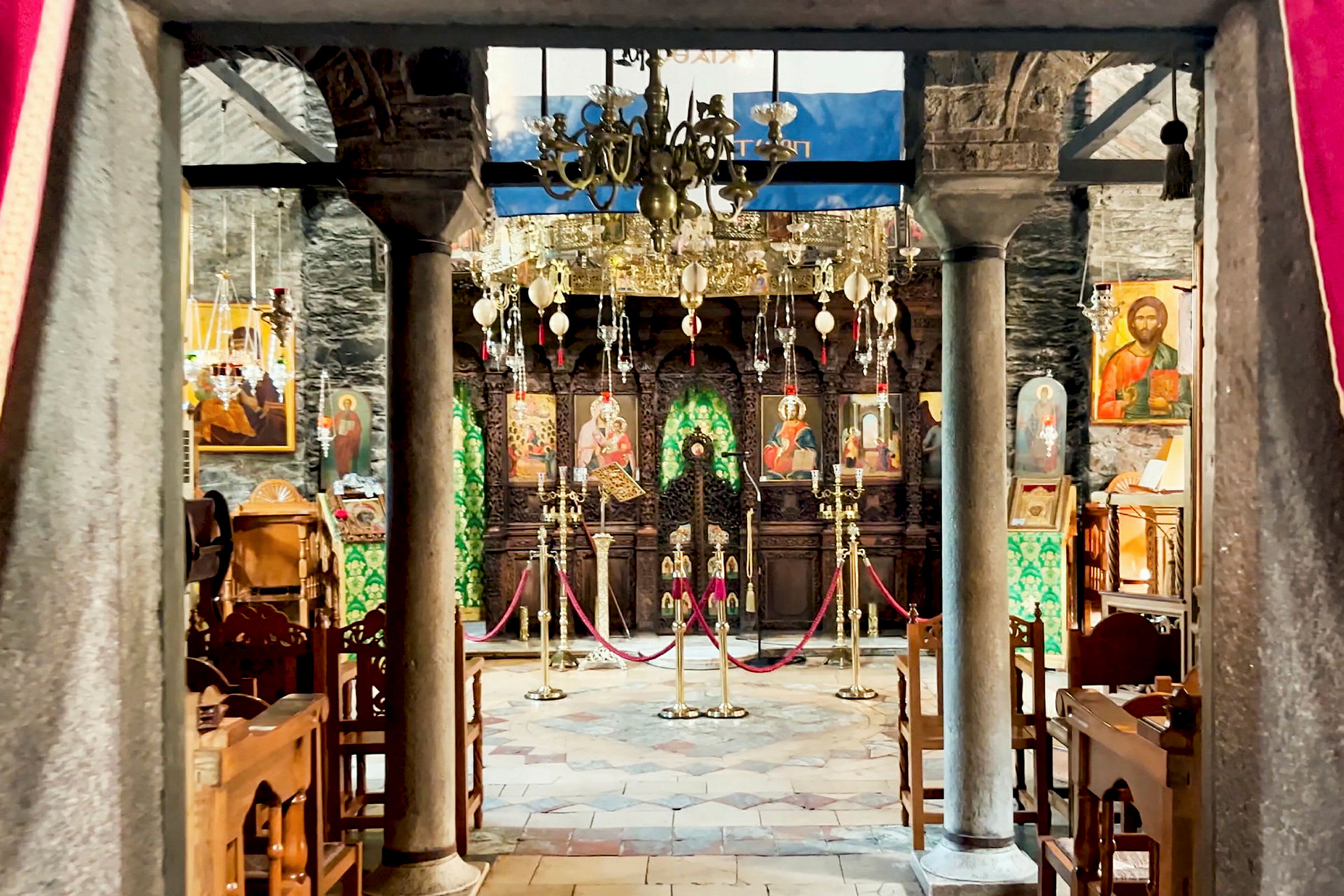 En interiör av en dekorerad kyrka med ikoner och ljuskronor. Bänkar och pelare framträdande. (AI-genererad text)