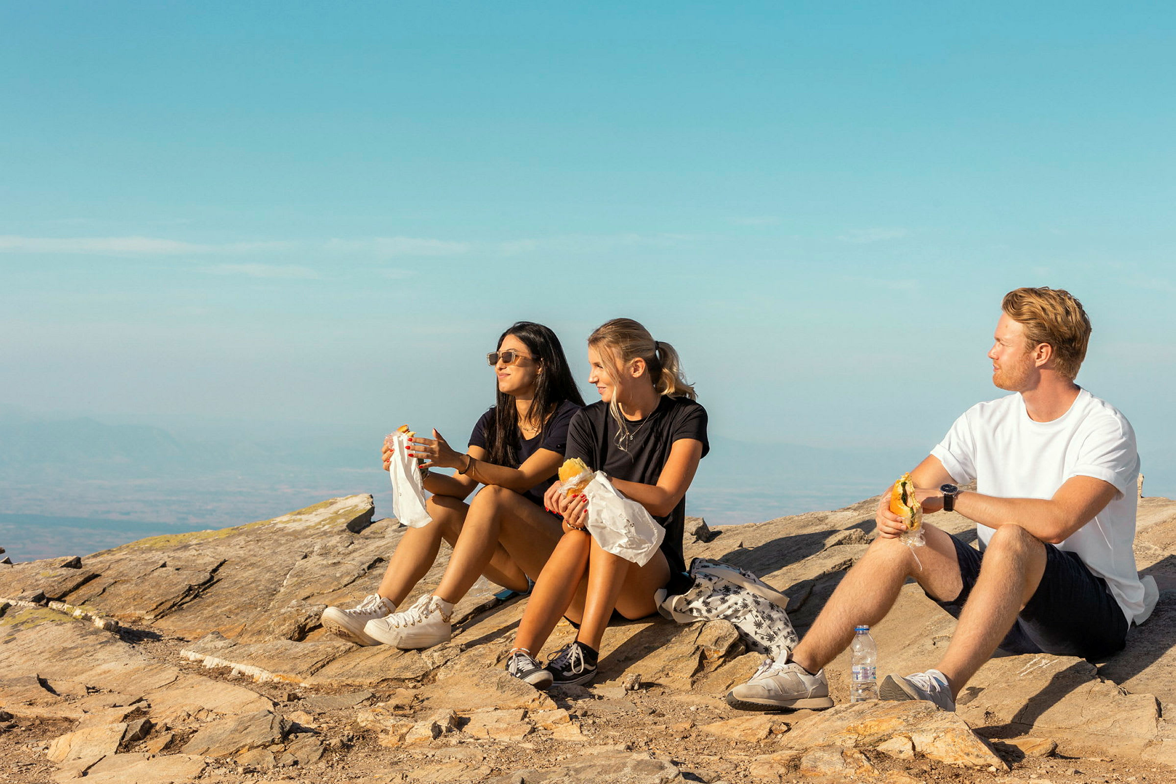 Tre personer sitter på en bergstopp och äter mat. (AI-genererad text)