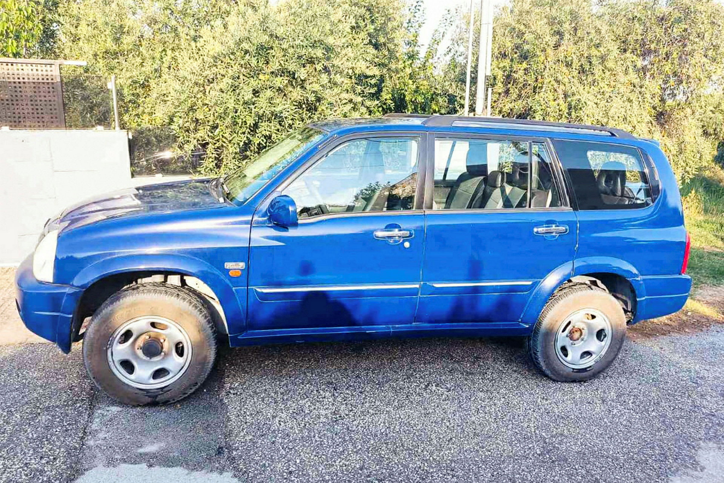 En blå SUV parkerad på en väg med träd i bakgrunden. (AI-genererad text)