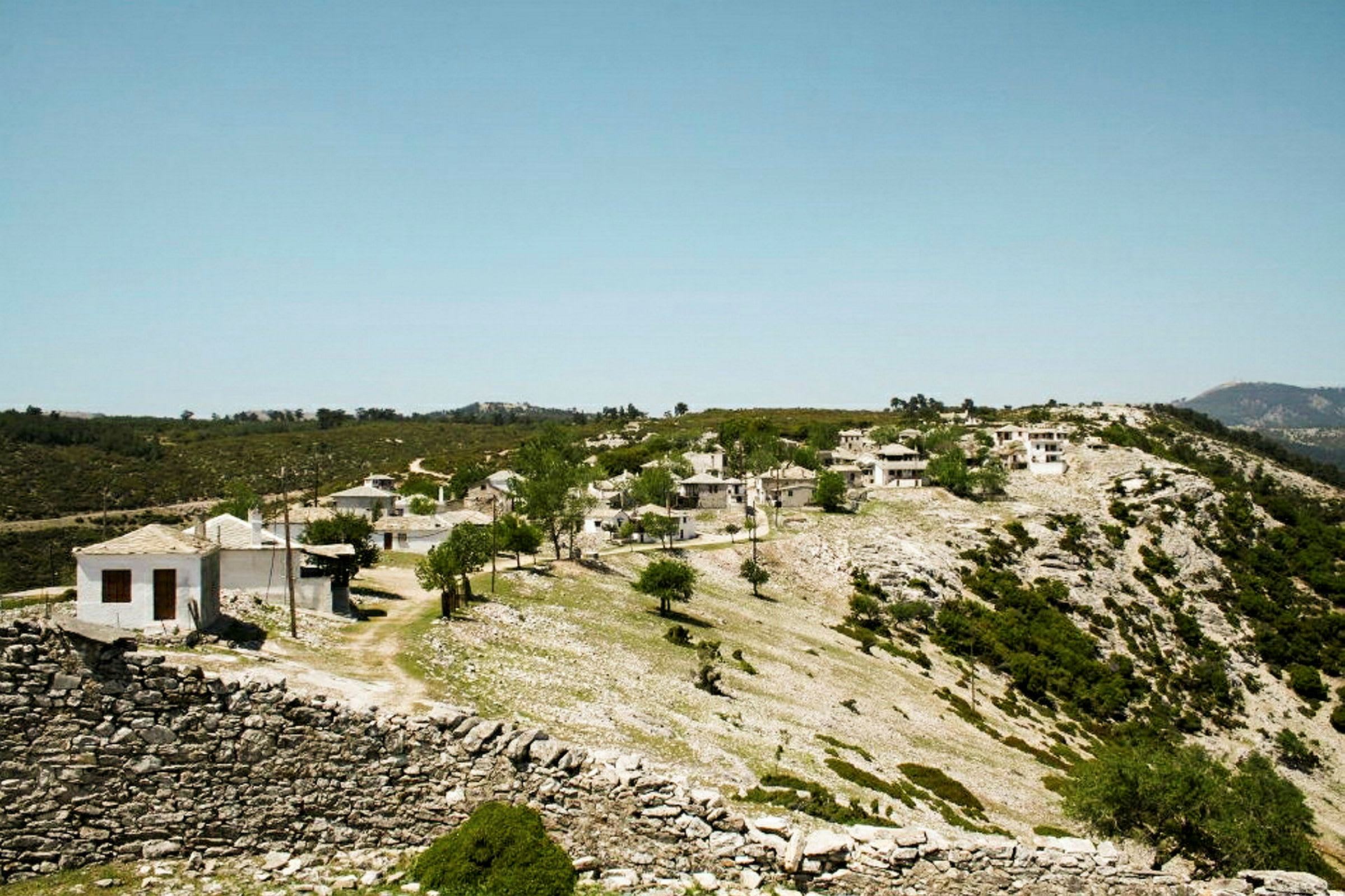En liten by ligger på en sluttning med vitmålade byggnader och omgiven av grön vegetation. (AI-genererad text)