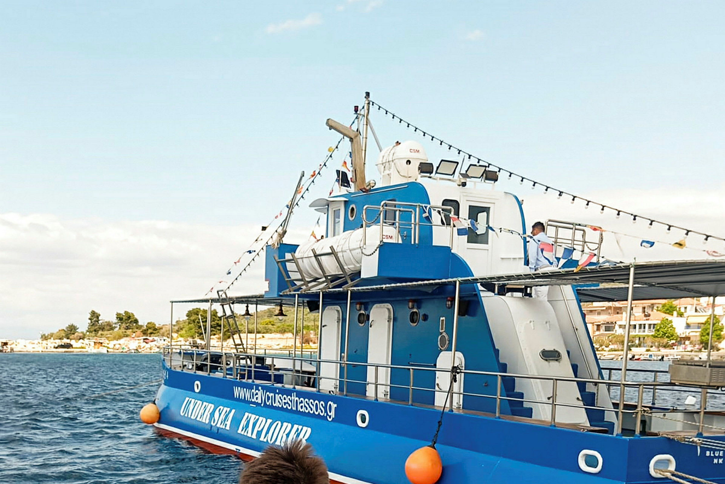 En blå båt med vita detaljer ligger vid kajen. Det finns även ett skylt med text på båten. (AI-genererad text)