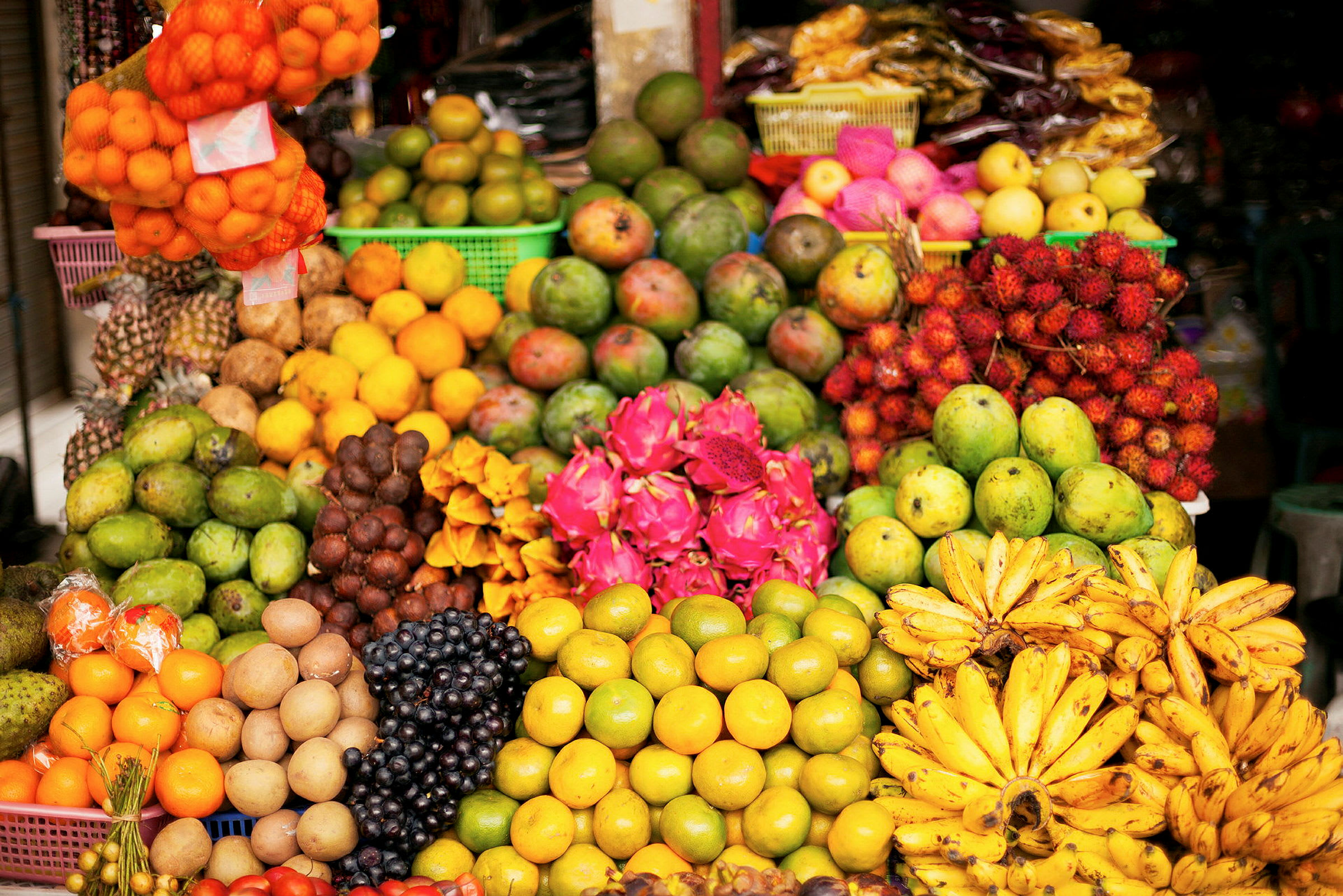 En färgglad display av olika frukter som mango, bananer, drakfrukt och andra på en fruktmarknad. (AI-genererad text)