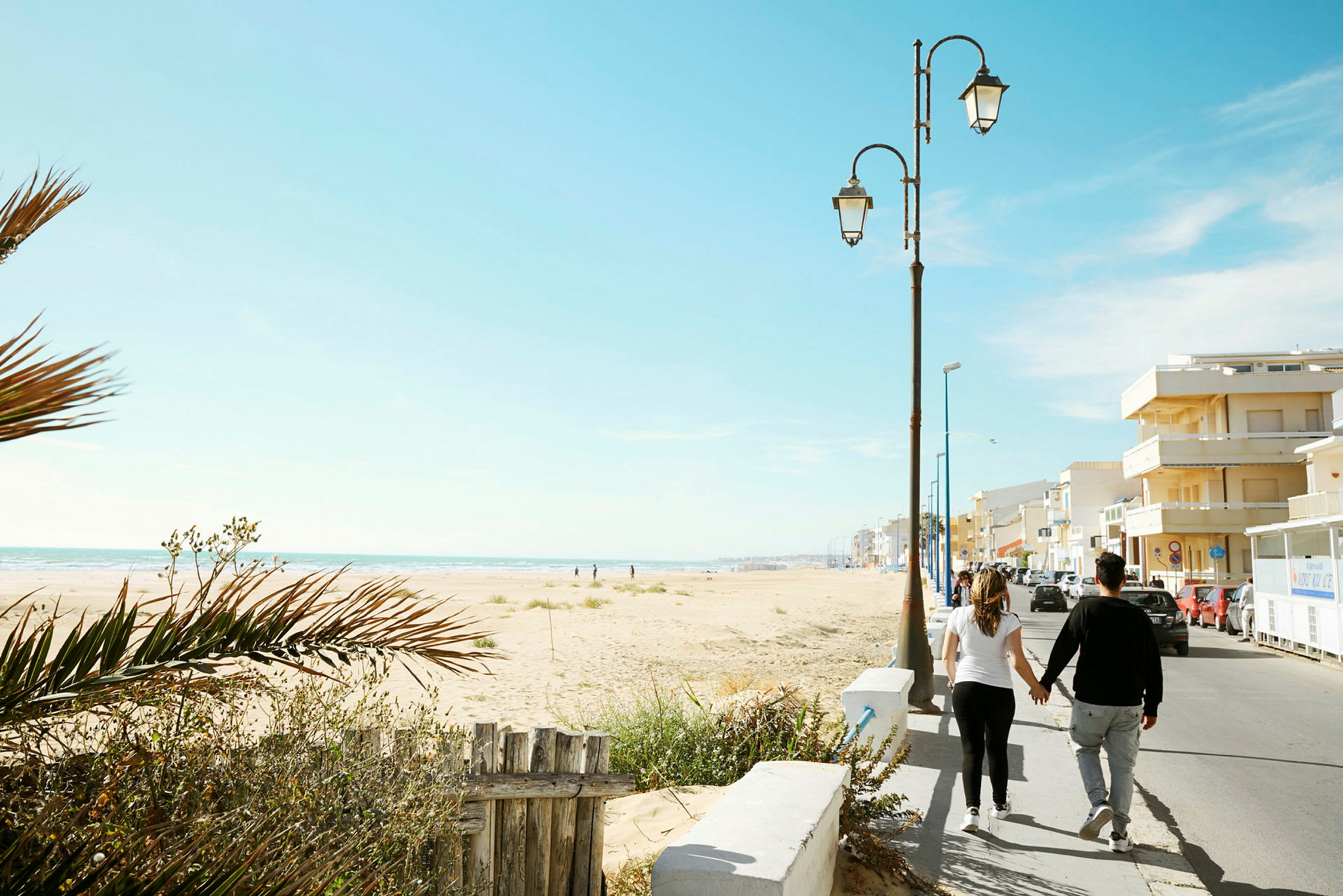 Man och kvinna promenerar hand i hand längs stranden vid en gata. (AI-genererad text)