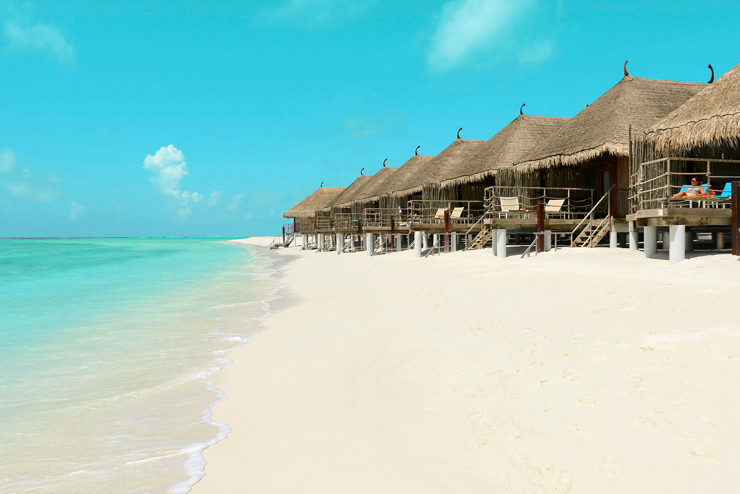 Strand med turkost vatten och bungalows på träpelare. (AI-genererad text)
