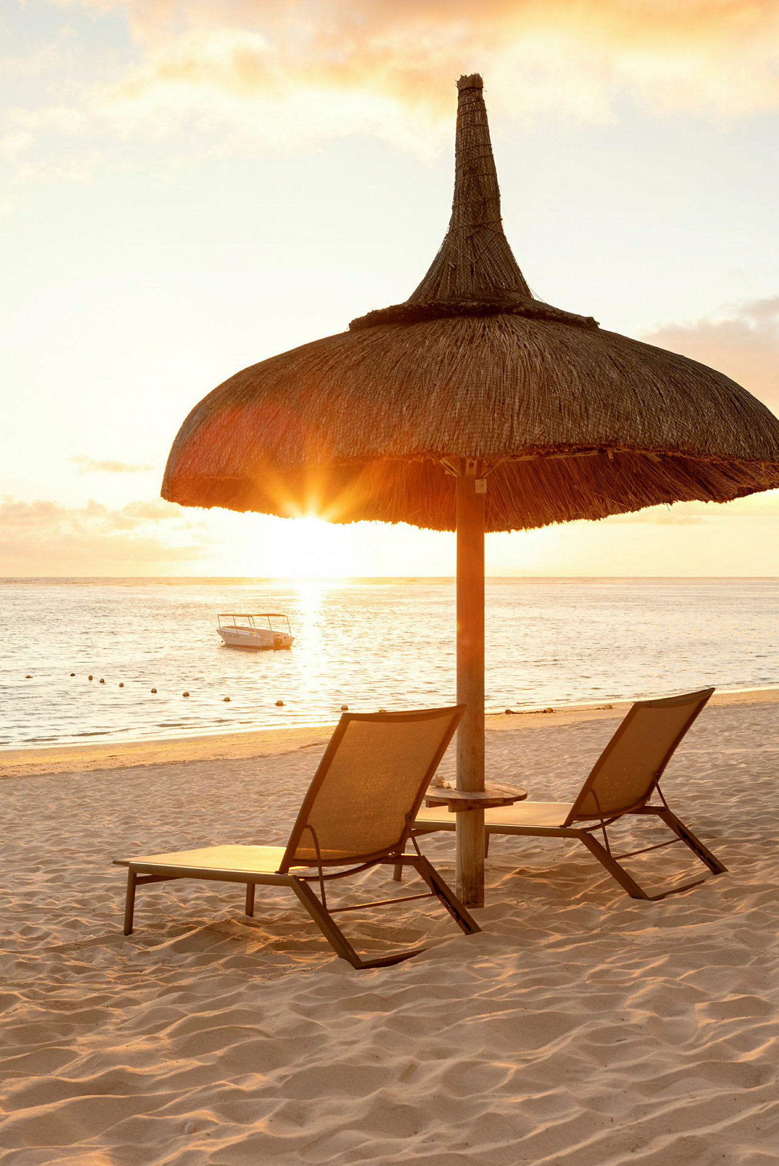 Solnedgång över strand med två solstolar och ett parasoll av trä och strå. (AI-genererad text)