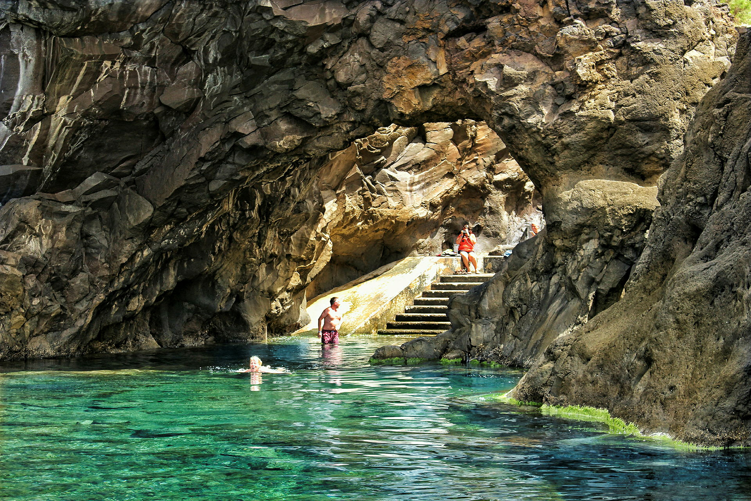 En naturlig klippgrotta med klart blått vatten och stentrappa. (AI-genererad text)