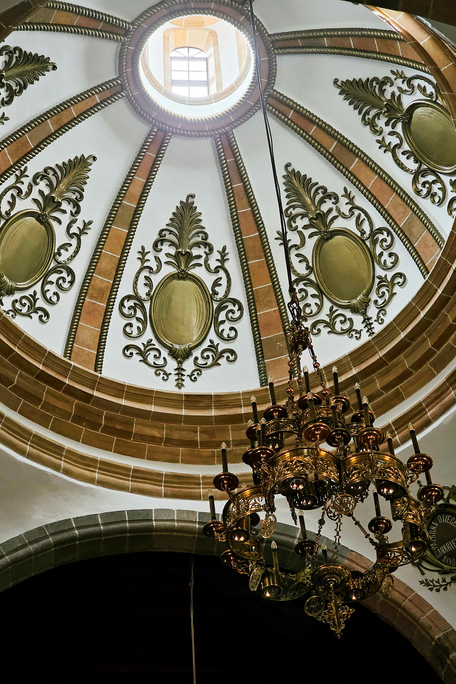 Interiören av en kupol med ornamenterad takdekoration och en ljuskrona. (AI-genererad text)