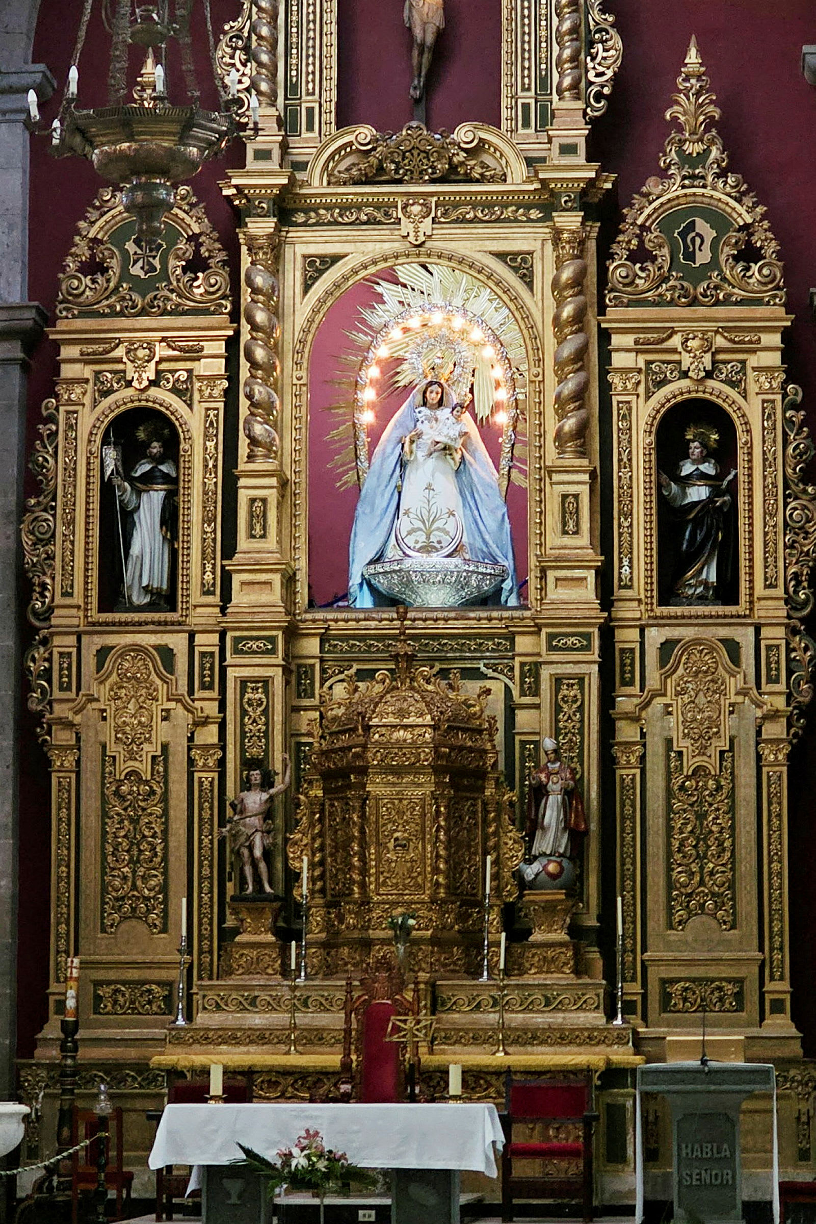Ett dekorerat altare i en kyrka med gyllene utsmyckningar och skulpturer. (AI-genererad text)