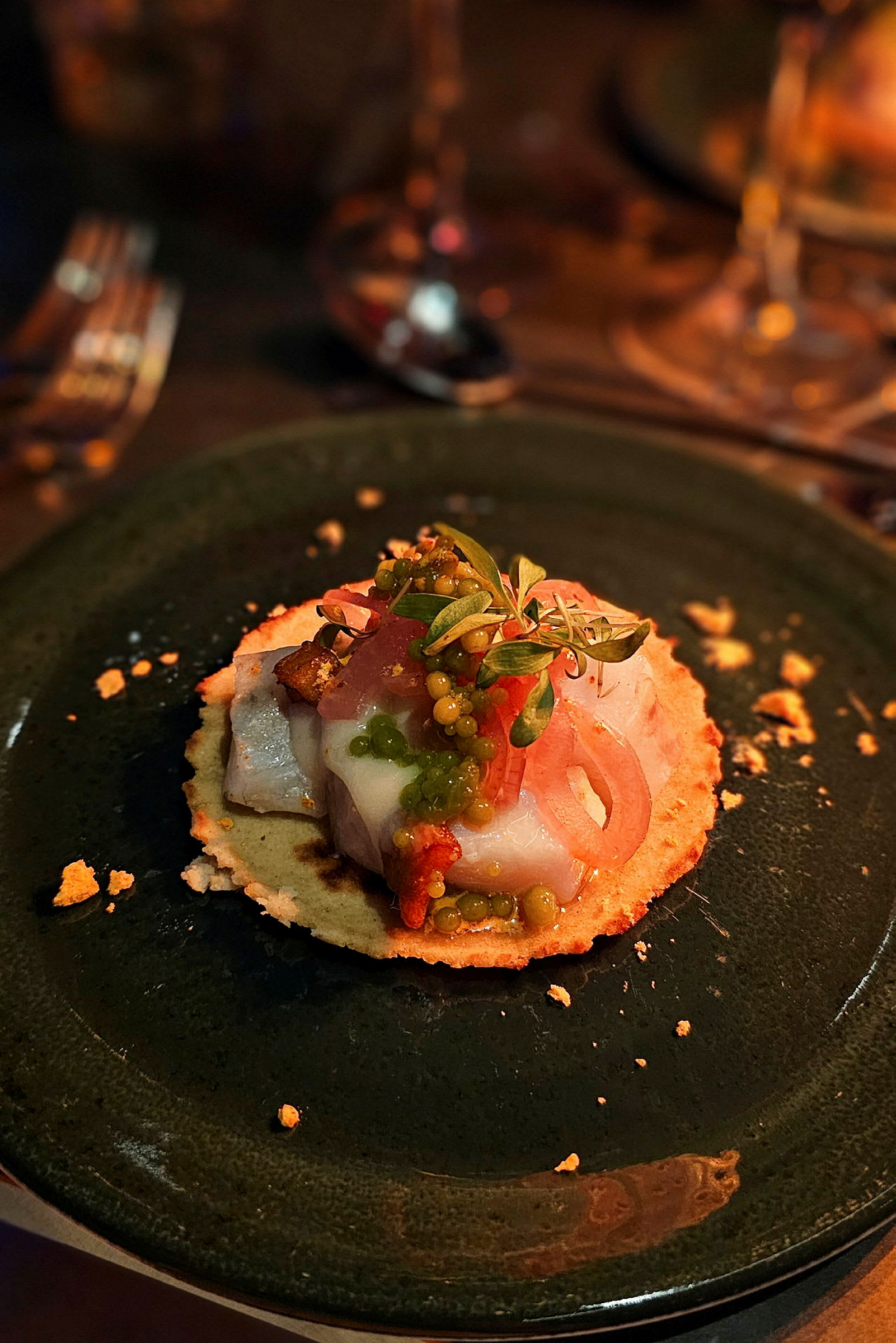 En tallrik med en gourmetförrätt innehållande tunn brödskiva toppad med fisk, grönsaker och örter. (AI-genererad text)